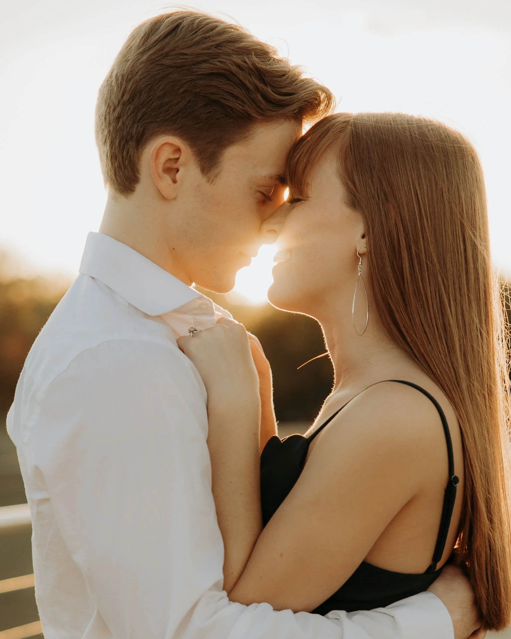 A young couple with foreheads touching, smiling, during sunset.