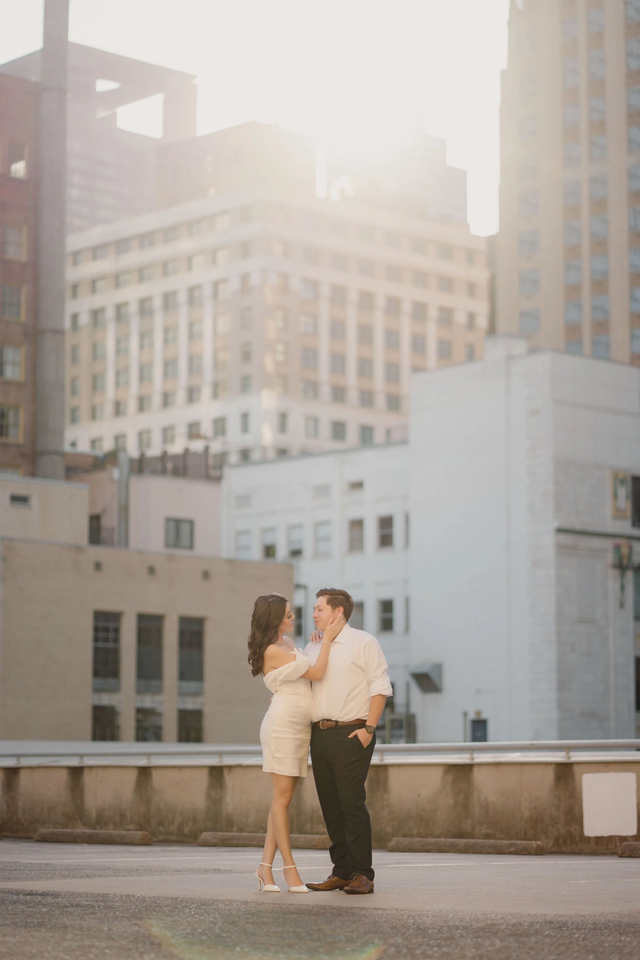 A couple standing close together on a city street at sunset, with tall buildings in the background.