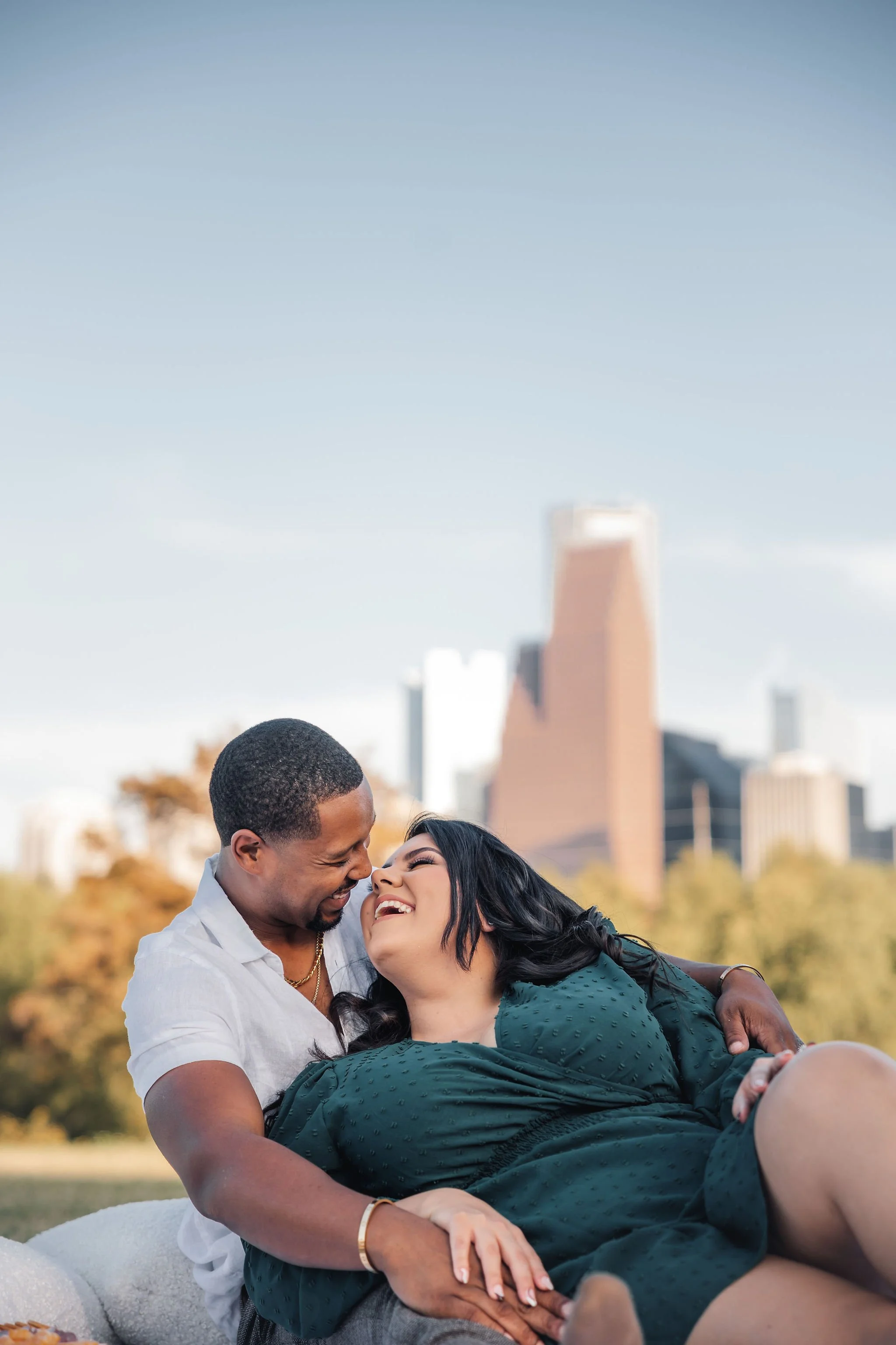 A happy couple laughing and embracing outdoors with a city skyline in the background.