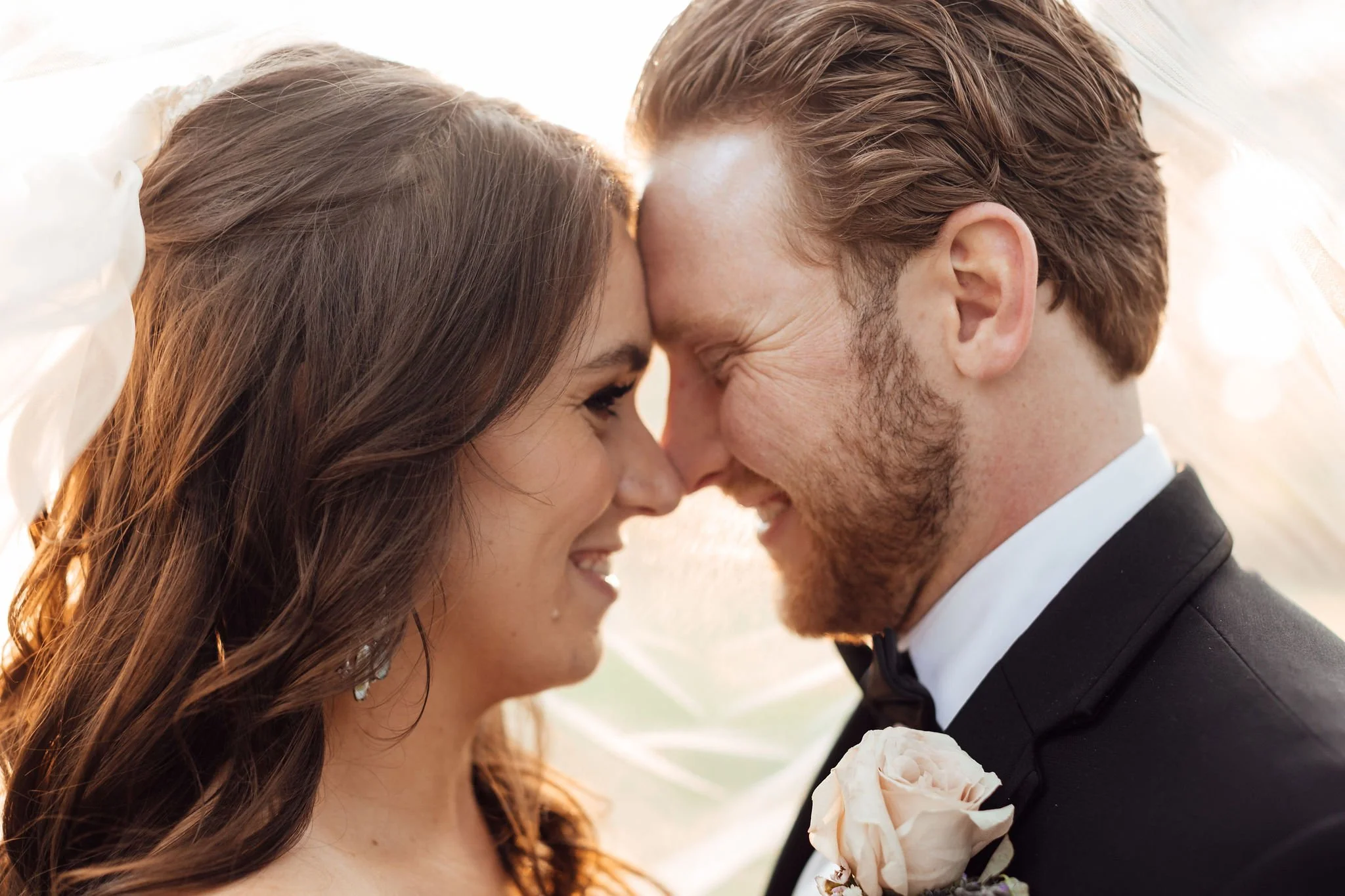 Close-up of a bride and groom leaning their foreheads and noses together, smiling at each other during their wedding.