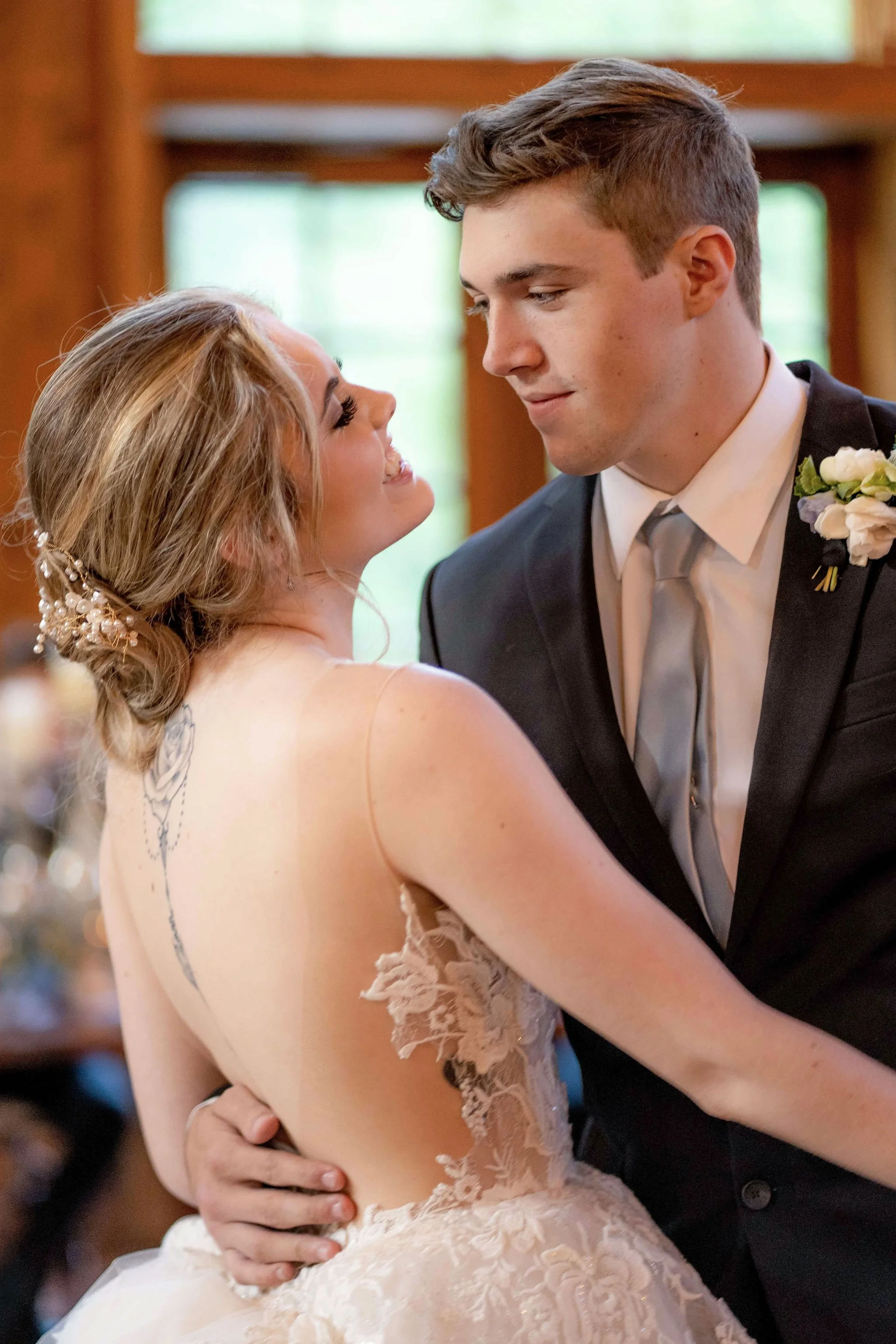 A bride and groom sharing a dance at their wedding. The bride has an updo hairstyle with floral hair accessories, and the groom is wearing a black suit with a white shirt and gray tie.