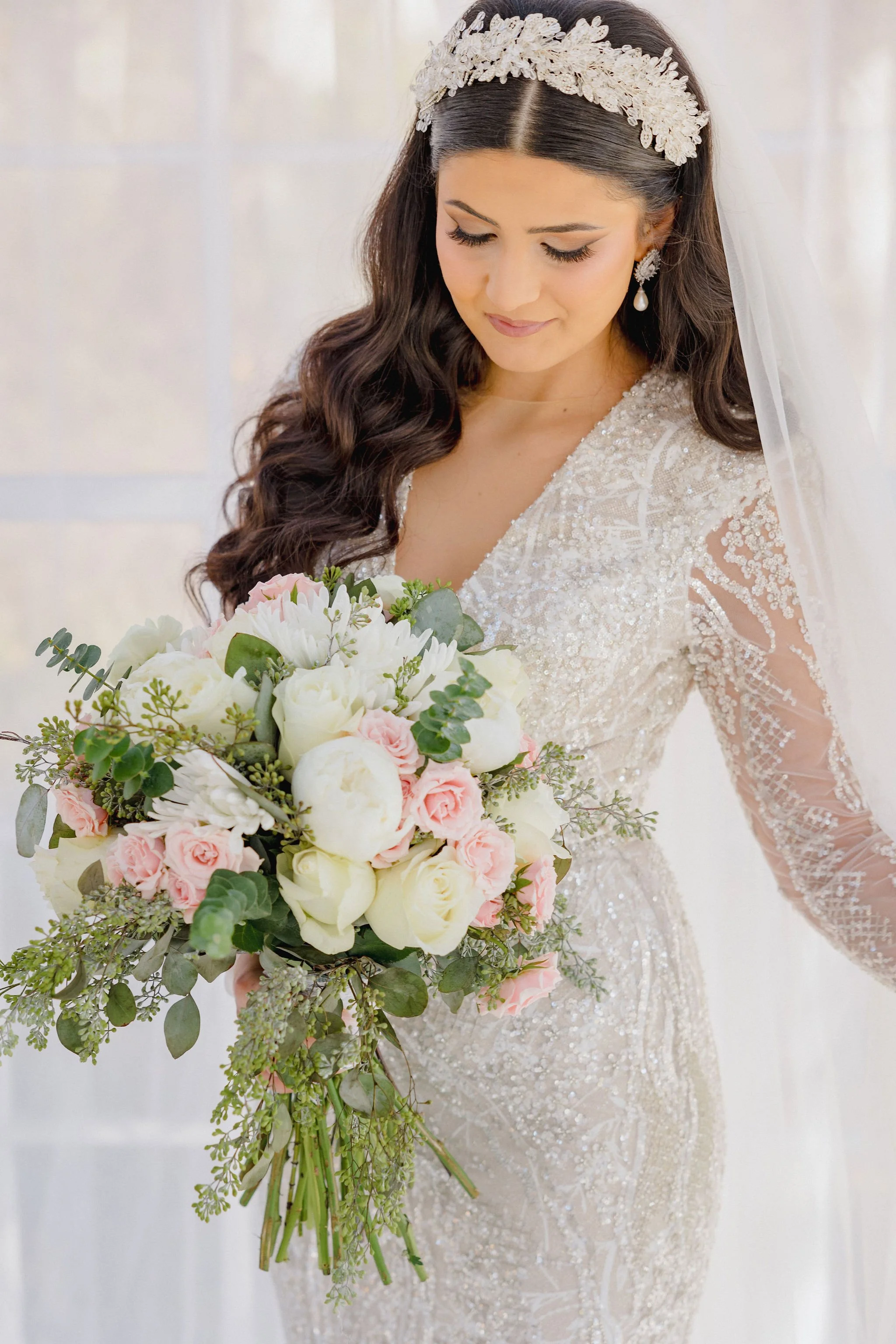 A bride in a detailed wedding dress holding a bouquet of white and pink roses with greenery.