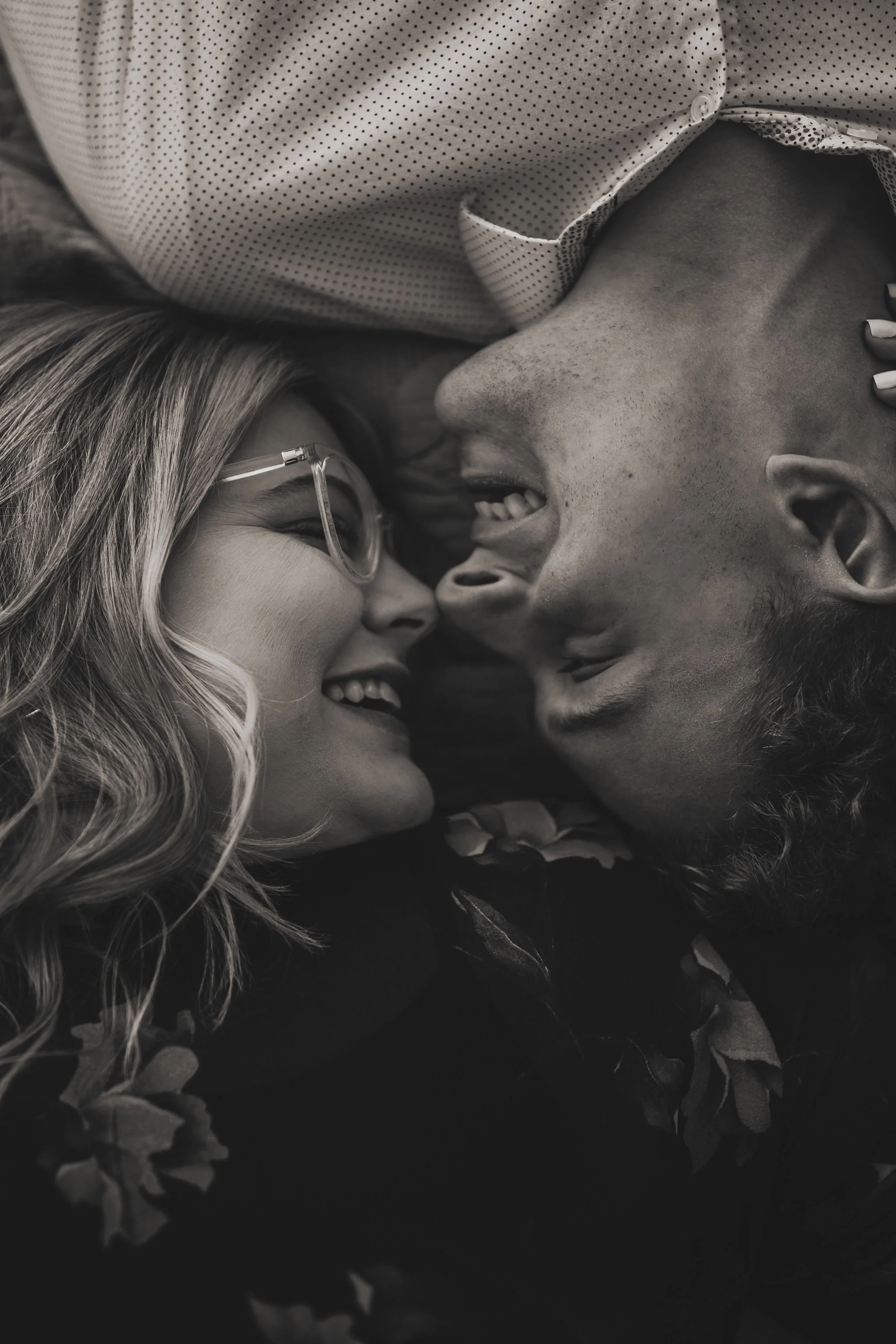 Black and white photo of a man and a woman lying face to face, smiling, with their foreheads touching, close together in a loving embrace.