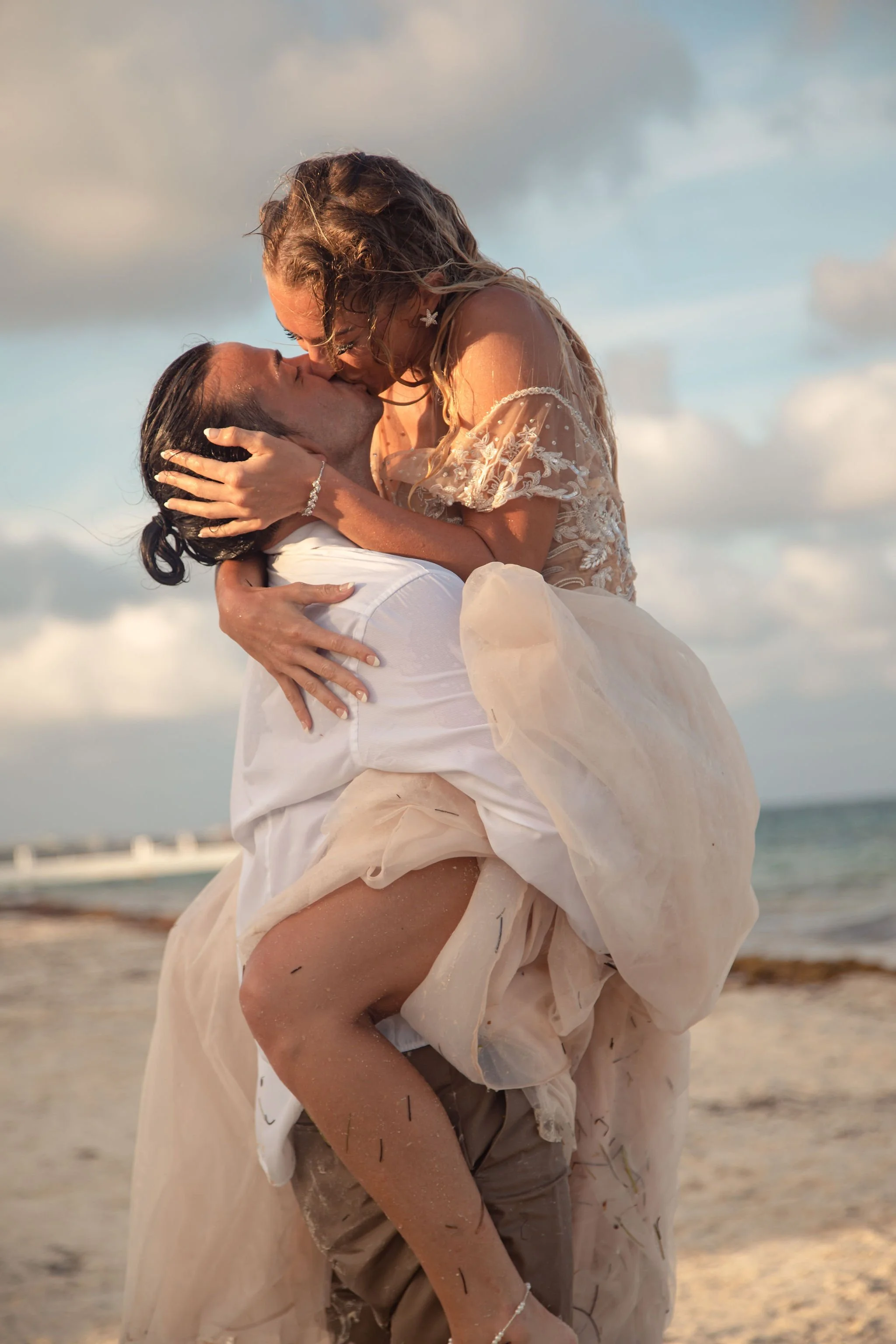 A couple kissing on the beach, the woman being carried by the man, during sunset.