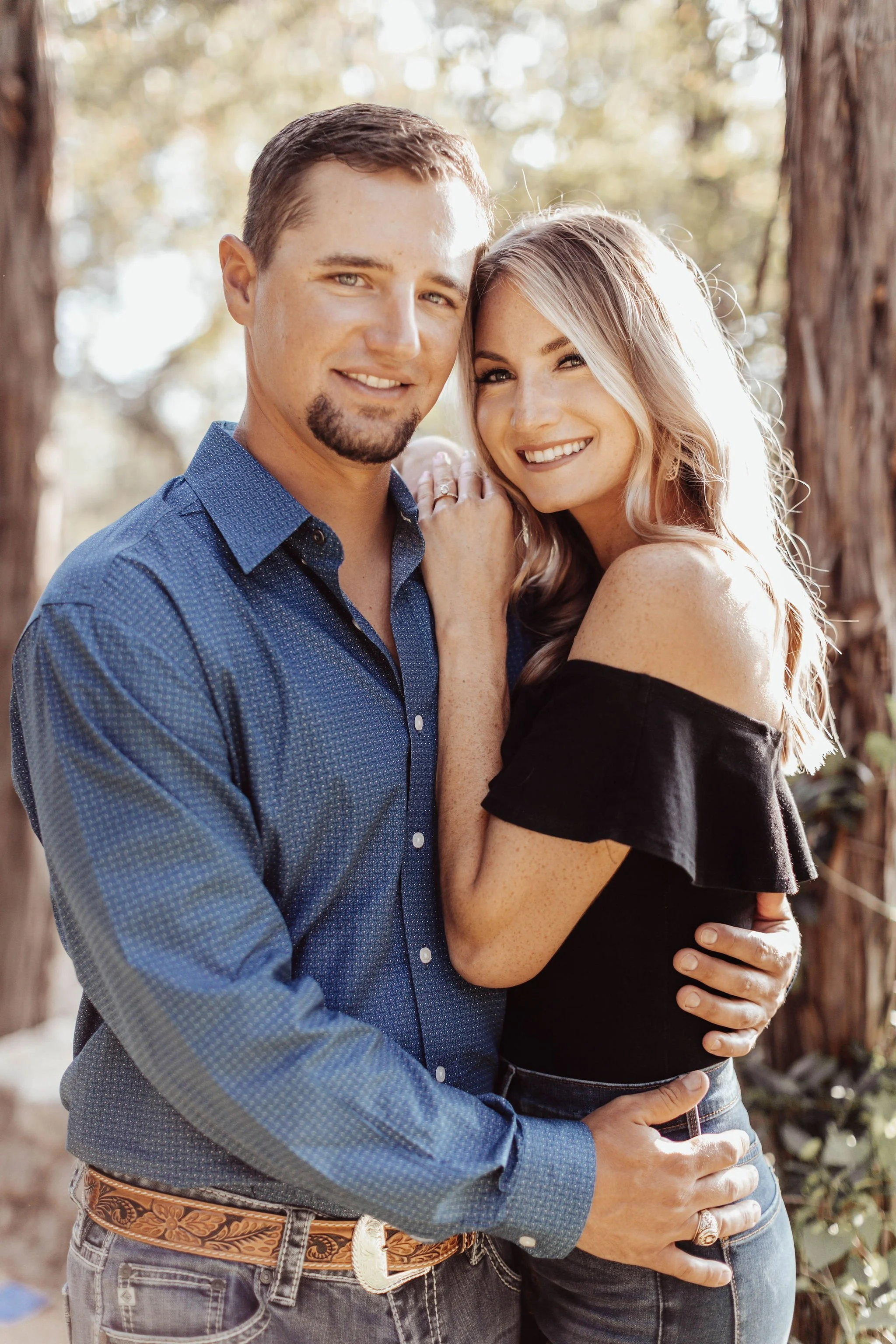 A happy couple smiling and embracing outdoors near trees.