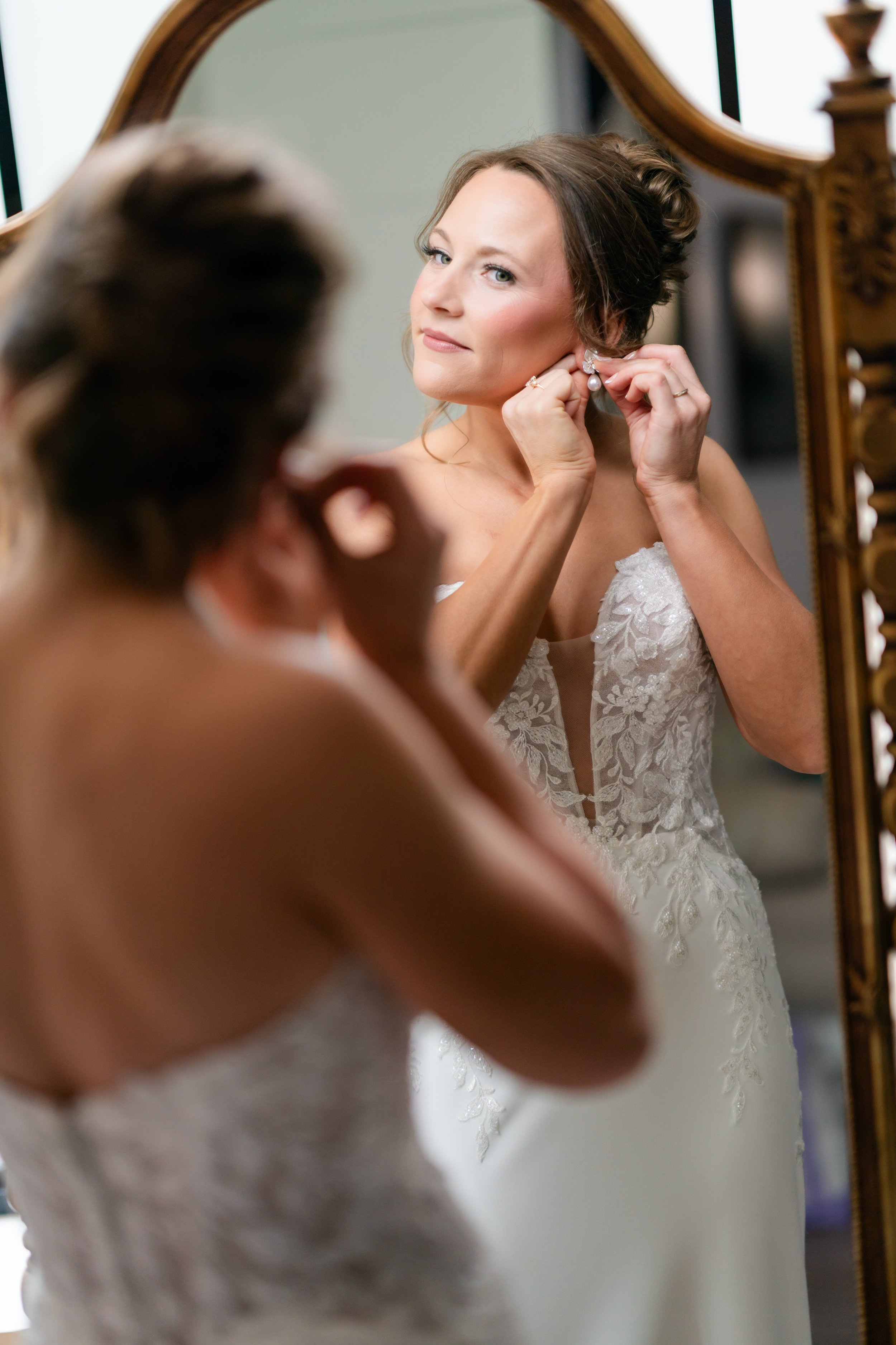 a woman adjusting her earrings while looking into the mirror