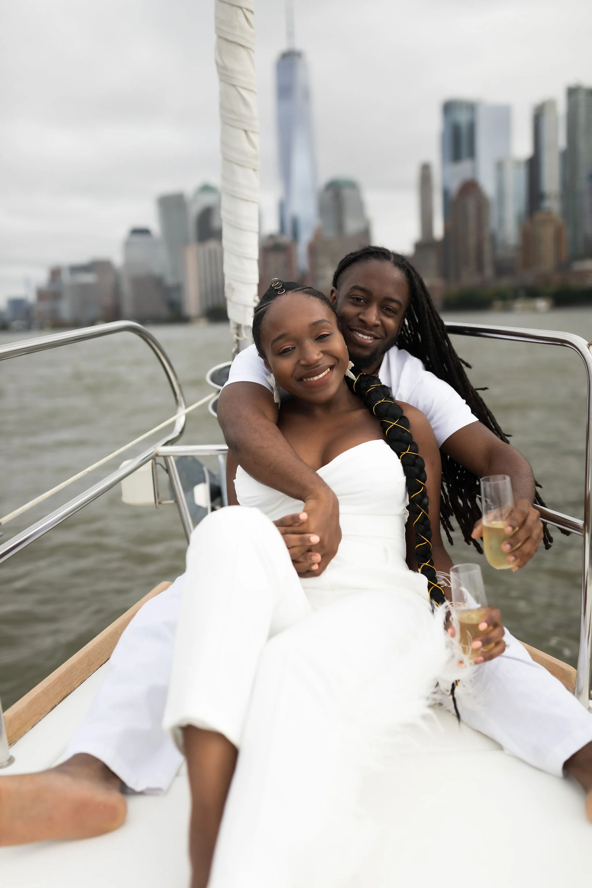 A happy couple enjoying a boat ride on the water with a city skyline in the background, holding glasses of champagne.