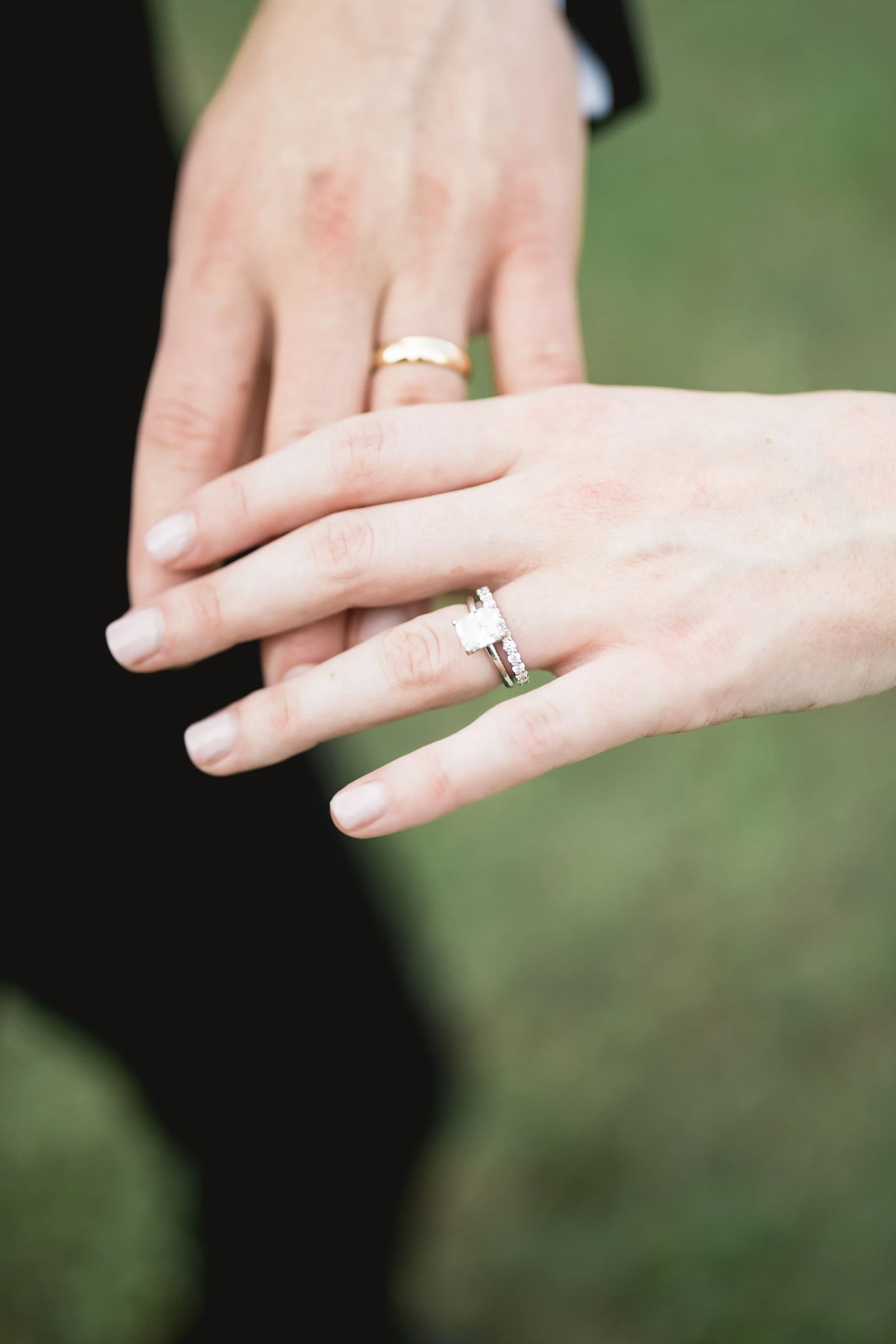 Close-up of two hands displaying wedding rings, with a blurred green background.