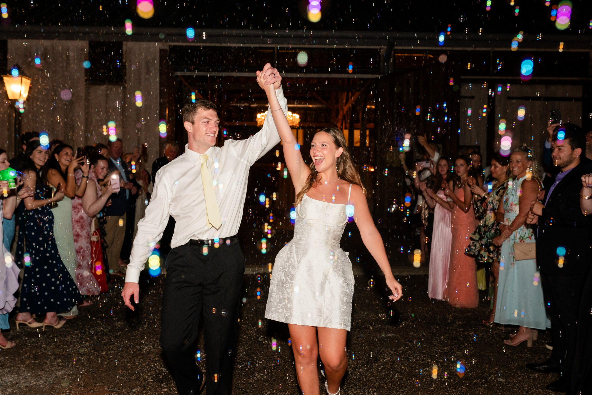 bride and groom leaving the reception while holding hands and having their loved ones cheer for them 