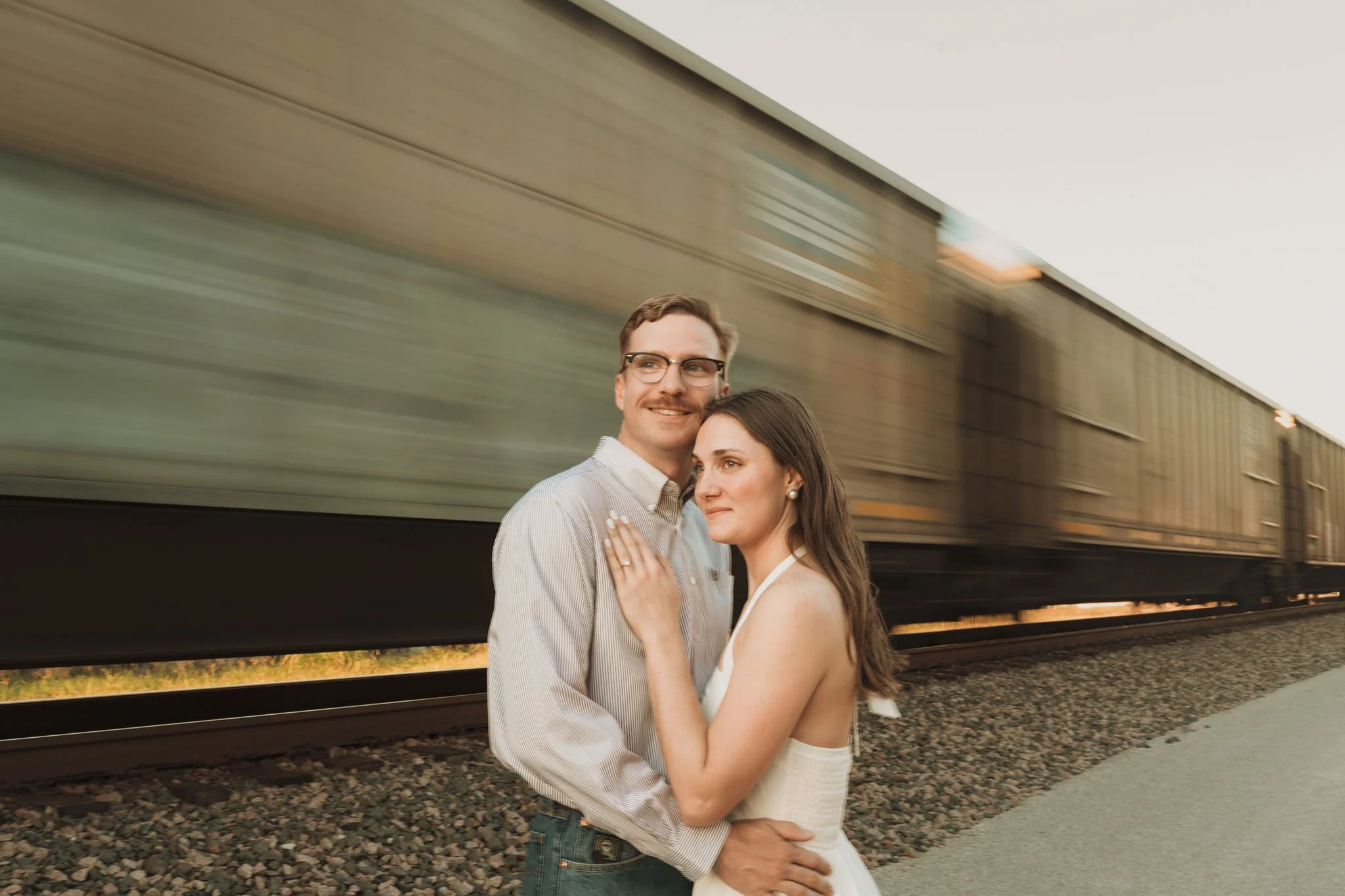 A couple embracing near a moving train outdoors during sunset