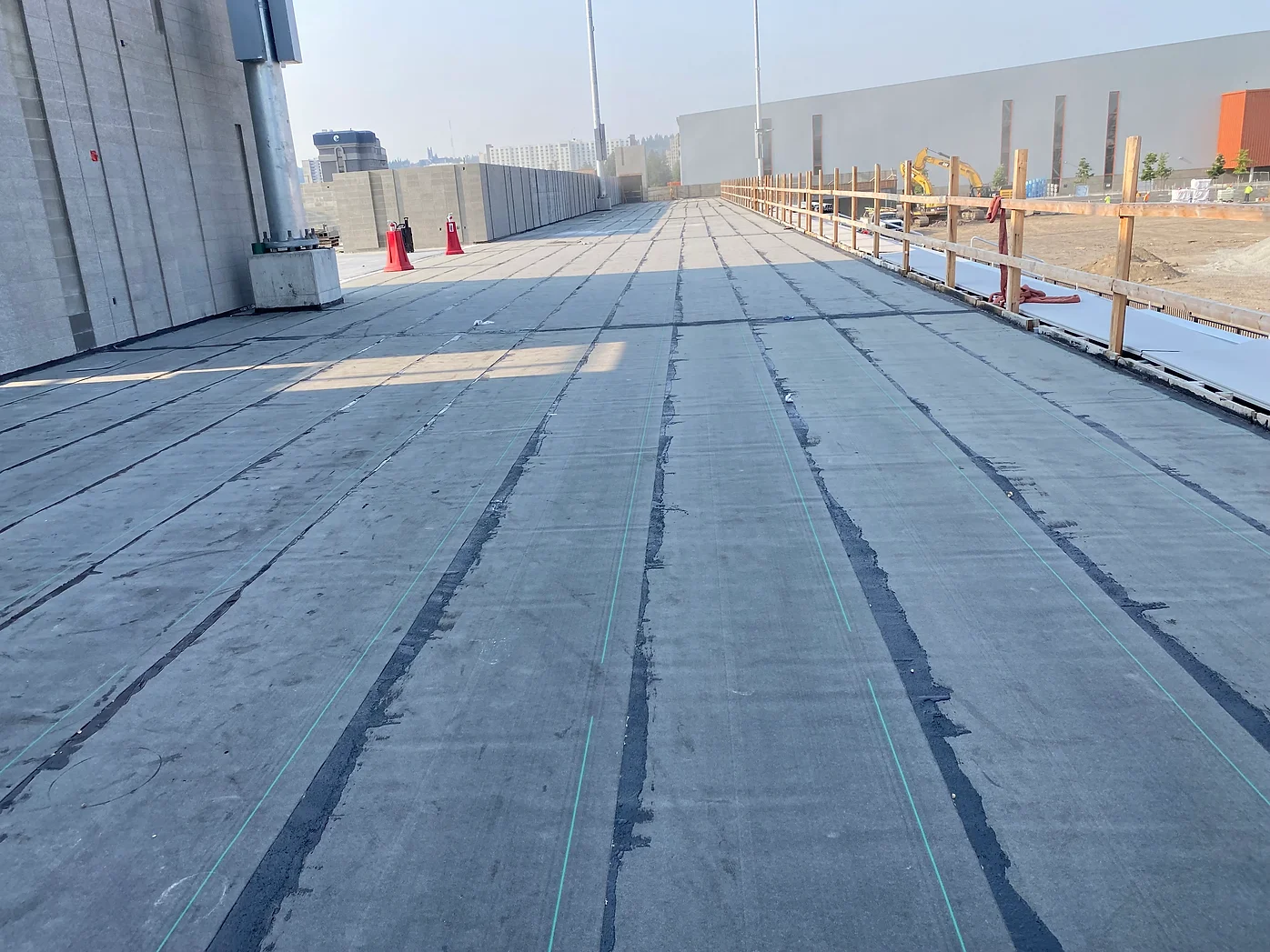 Large concrete surface under construction with barriers and equipment, adjacent to a building.