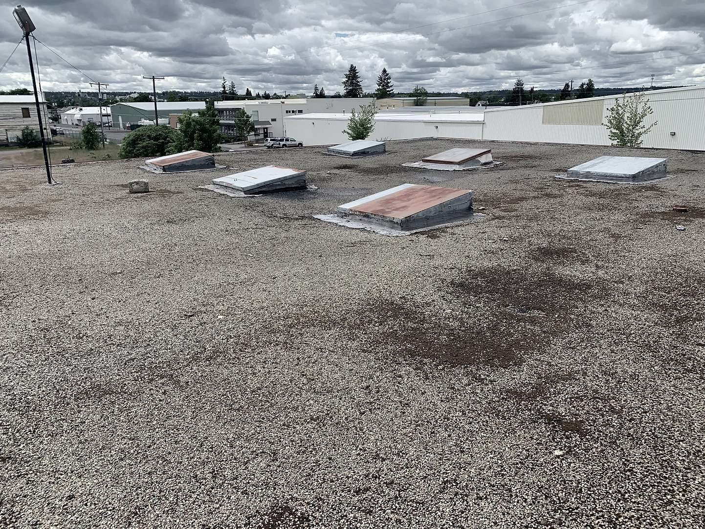 Gravel rooftop with several rectangular skylights and a cloudy sky background.