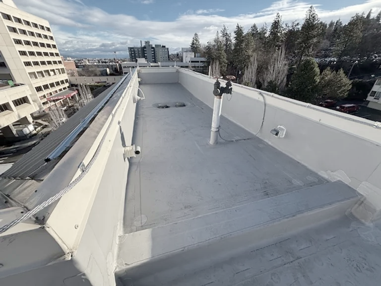 Flat rooftop with equipment, surrounded by buildings and trees