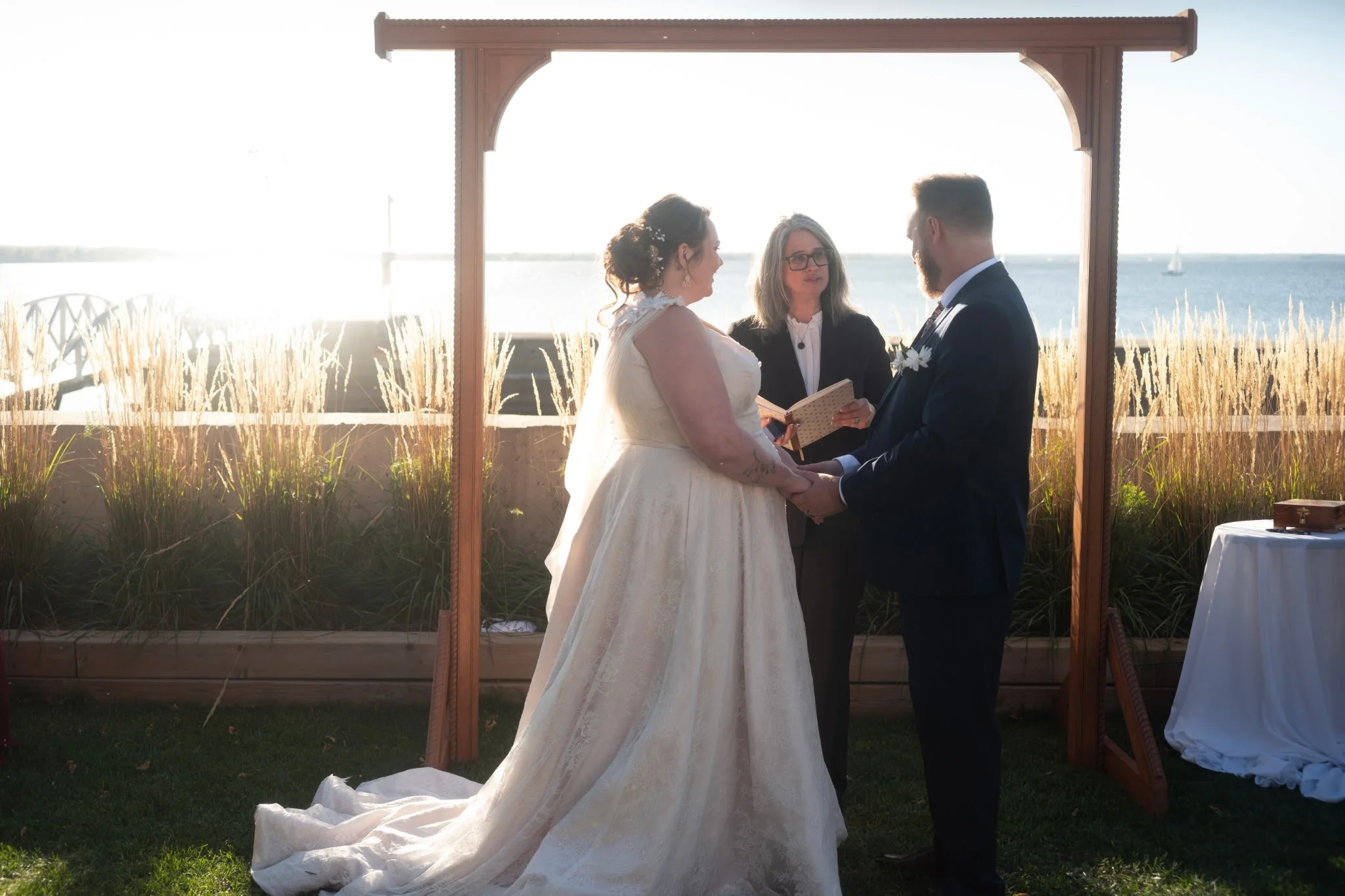 Nadia Pruett Officiant standing at an altar with a bride in a flowing white dress and a groom in a tuxedo at sunset by the water