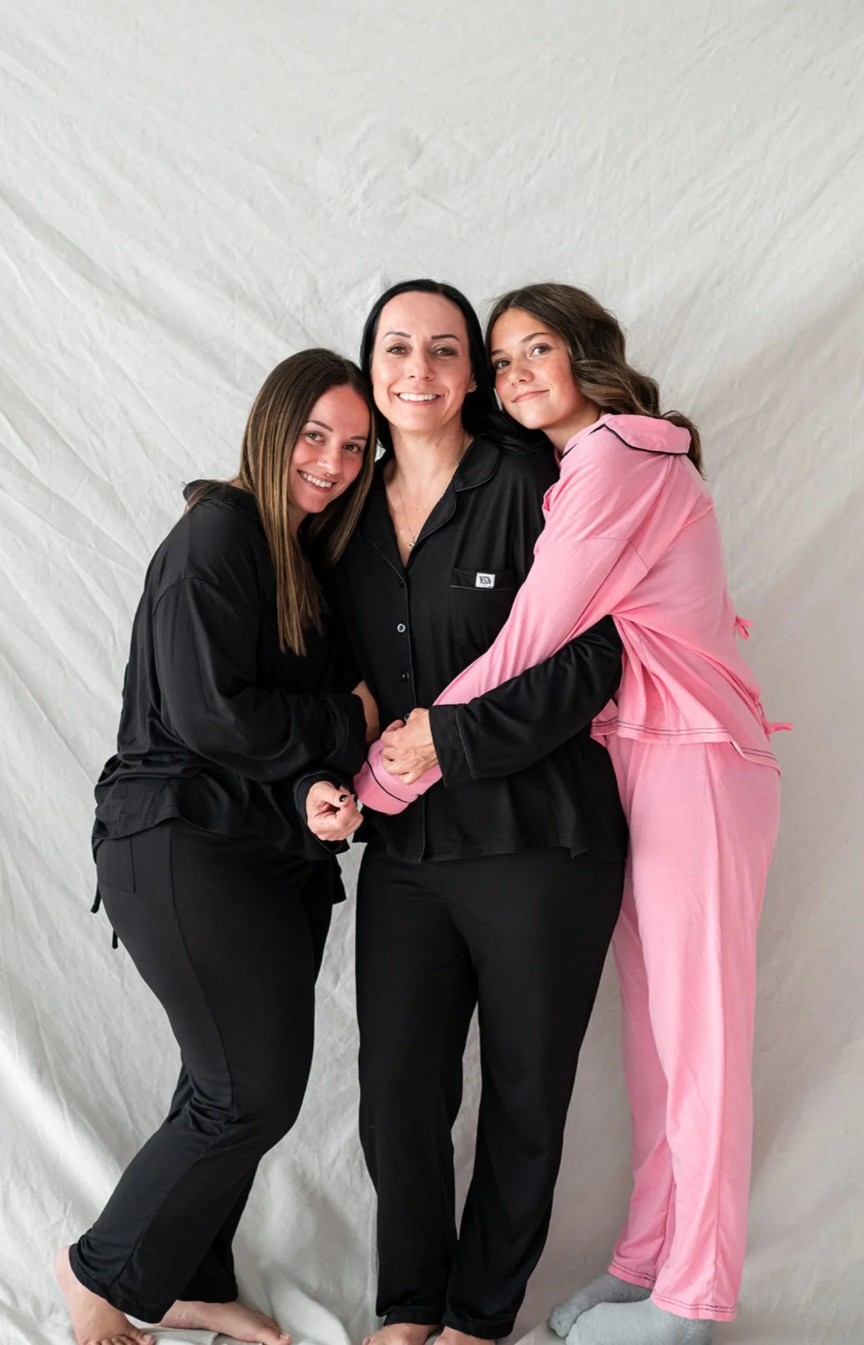 Three women in pajamas happily hugging each other against a white backdrop.