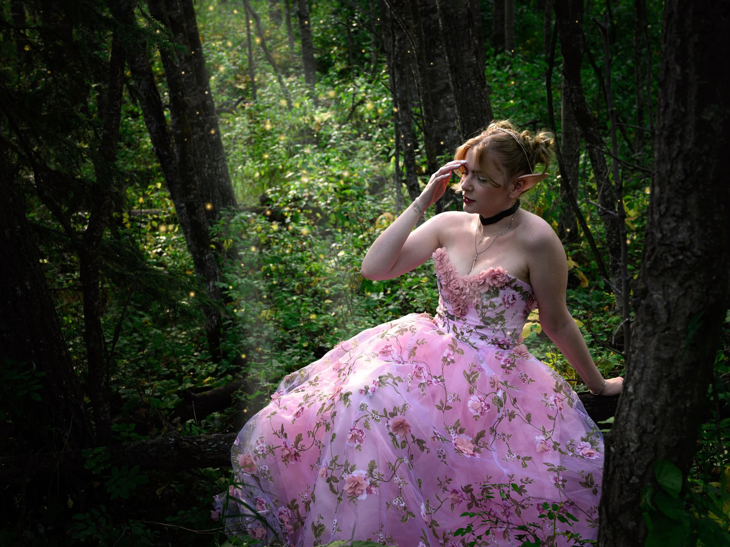 Fantasy photo taken in a forest outside of Edmonton of a fae princess in a pink floral gown, she has pointed ears and is seated on a log surrounded by streams of sunlight.