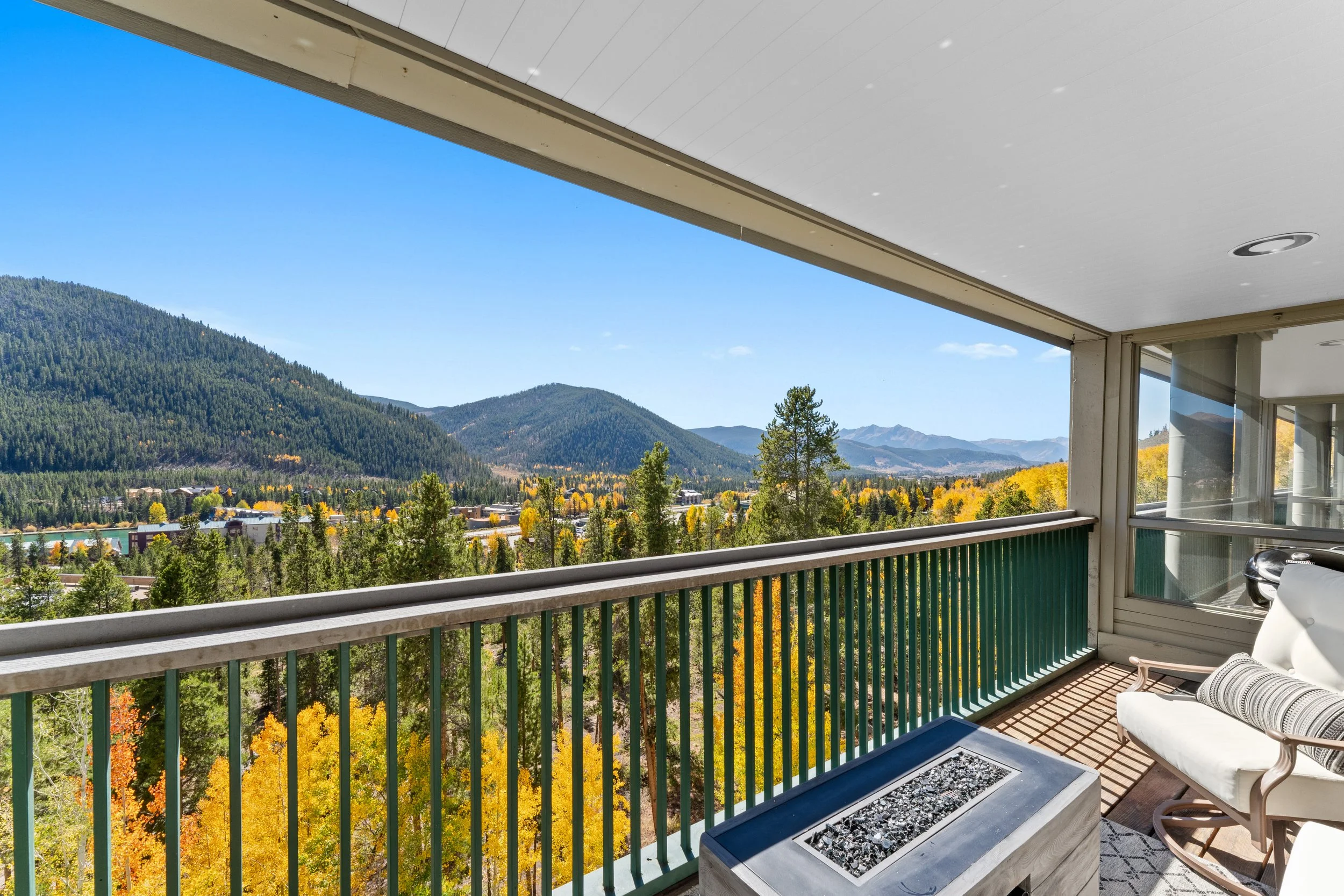 Balcony overlooking a scenic mountain view with trees, colorful fall foliage, and distant hills, partially covered by a white ceiling and enclosed by glass windows.