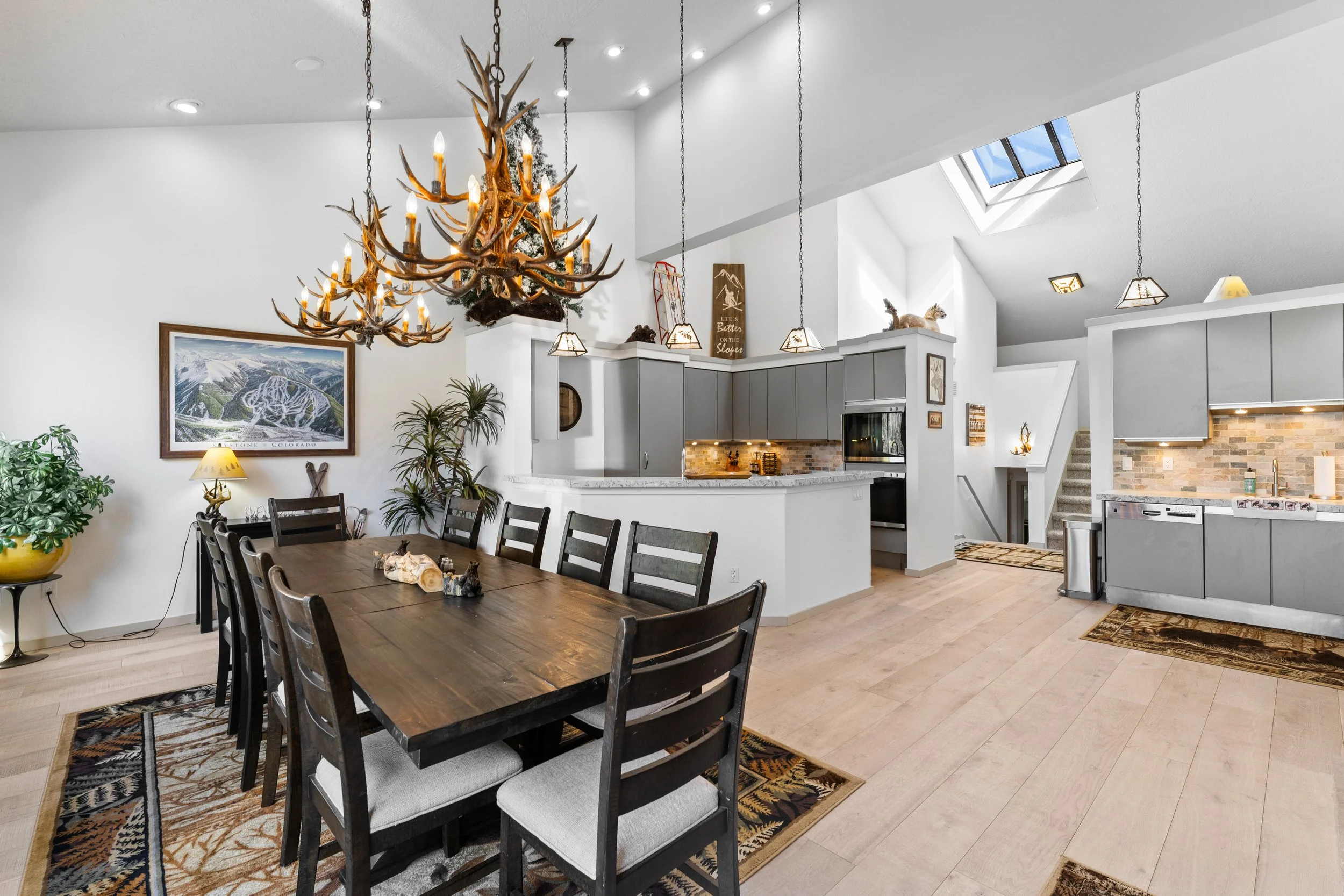 Open concept dining and kitchen area with rustic decor and antler chandelier.