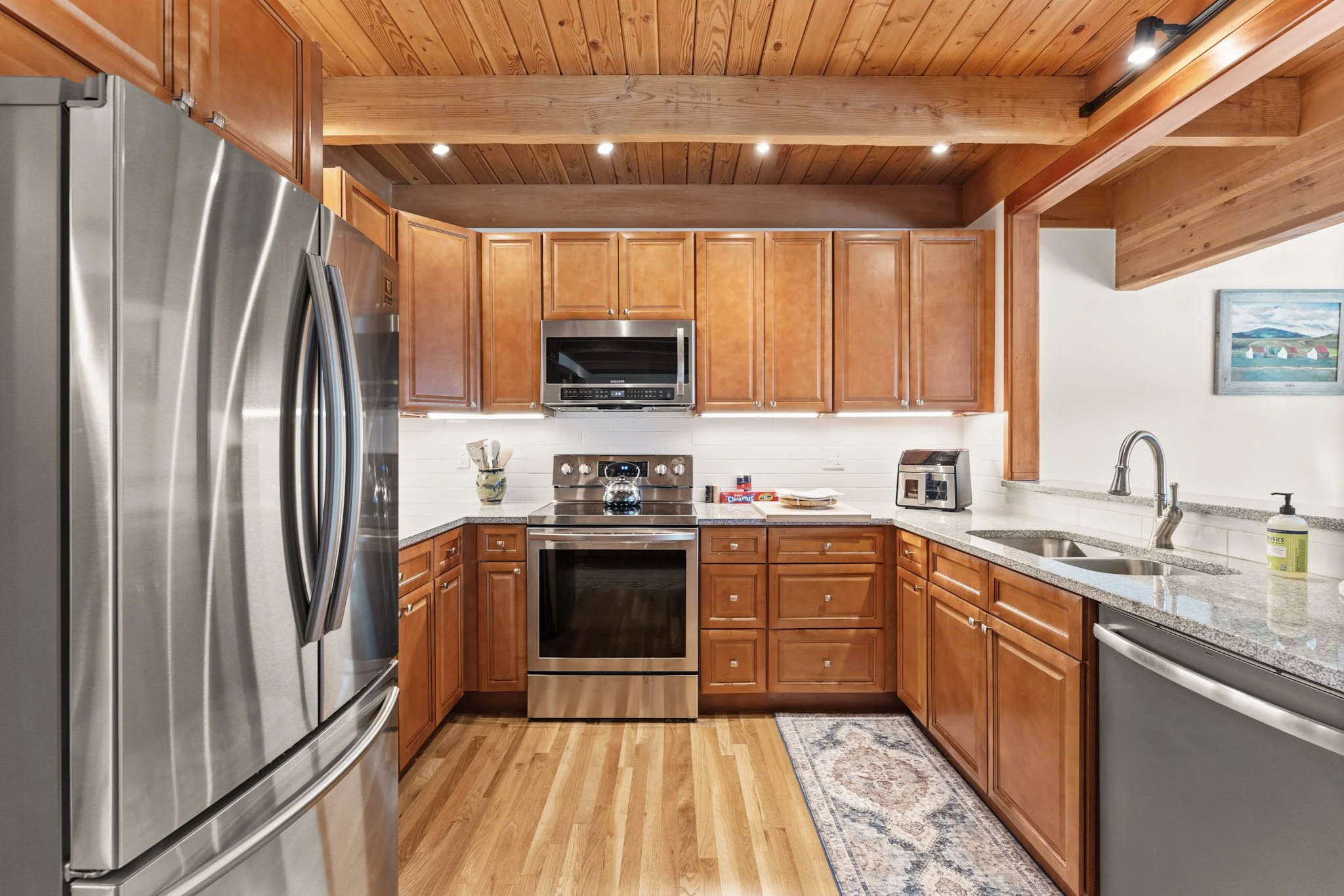 Modern kitchen with wooden cabinets, stainless steel appliances, granite countertops, and hardwood flooring.