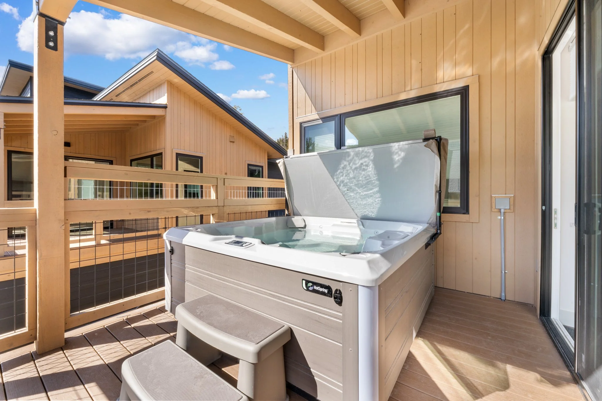 A hot tub on an outdoor balcony with a wooden railing and neighboring houses visible in the background on a sunny day.