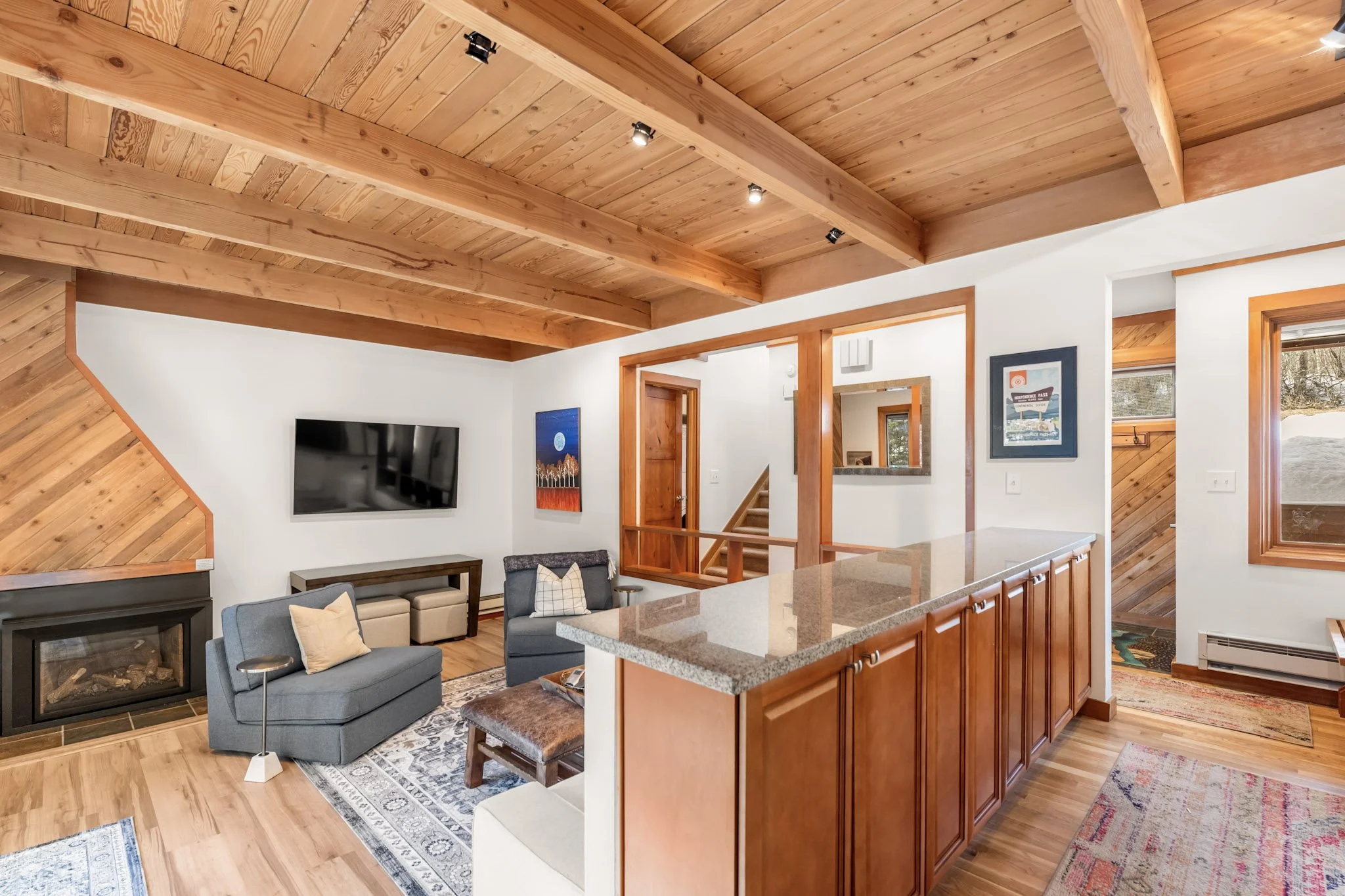 Living room with wooden ceiling and trim, two gray armchairs, a TV on the wall, a fireplace, and windows showing snow outside.