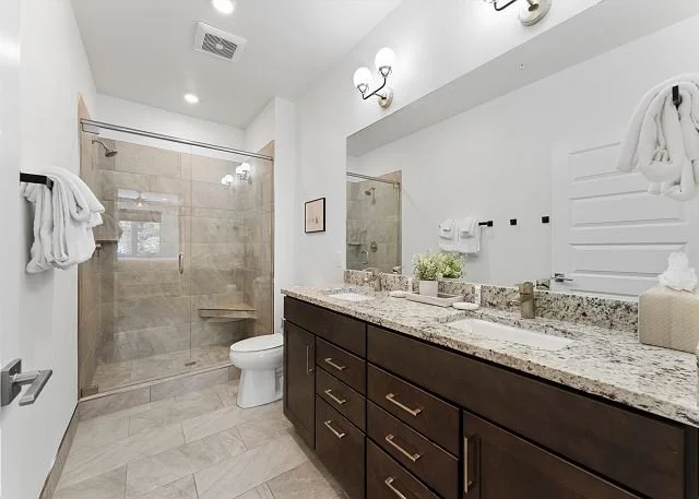 Bathroom with glass-enclosed shower, white toilet, dark wood vanity with granite countertop, towels, and decor.