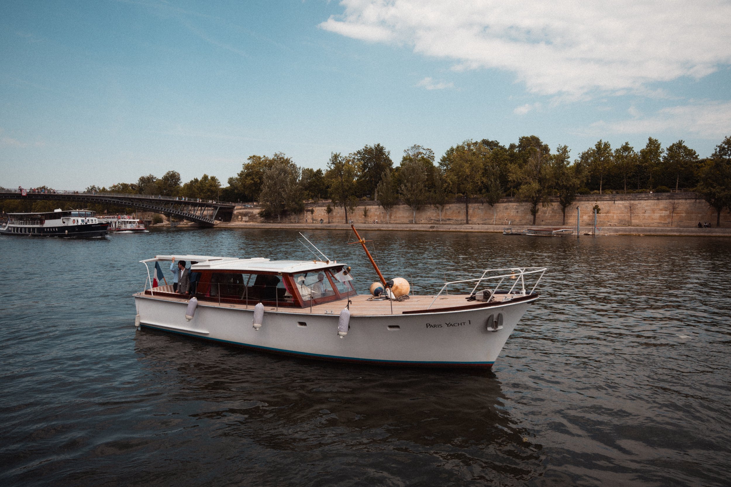 Un bateau à moteur sur la Seine à Paris avec un pont et une allée bordée d'arbres
