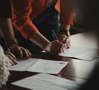 People signing documents on a dark wooden table.