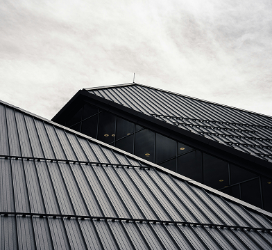 Close-up of a modern building's corner with metal siding and large glass windows under a cloudy sky.