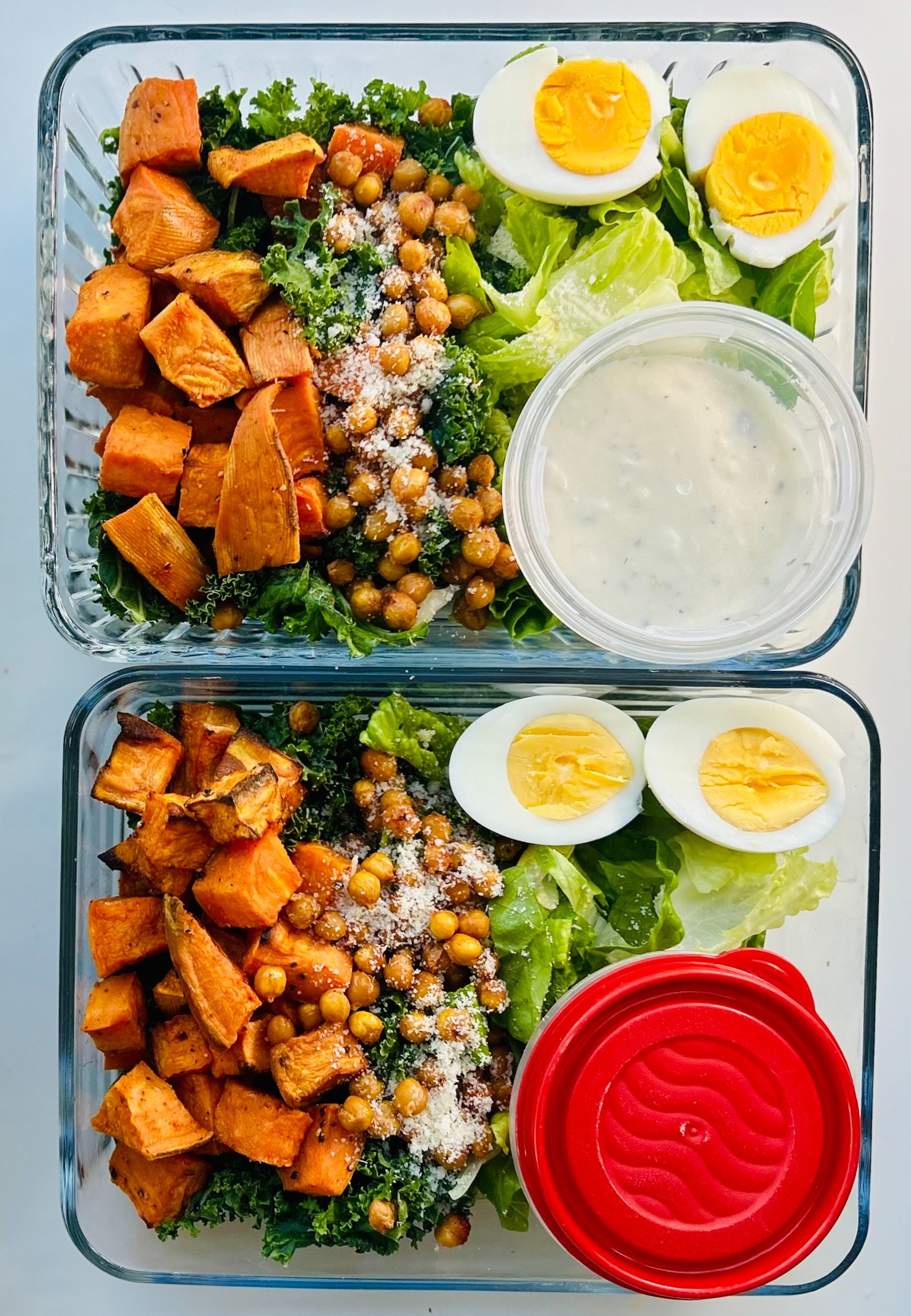 Meal-prep containers with Caesar salad, roasted yams, crispy chickpeas, boiled eggs, and Greek yogurt dressing on the side.
