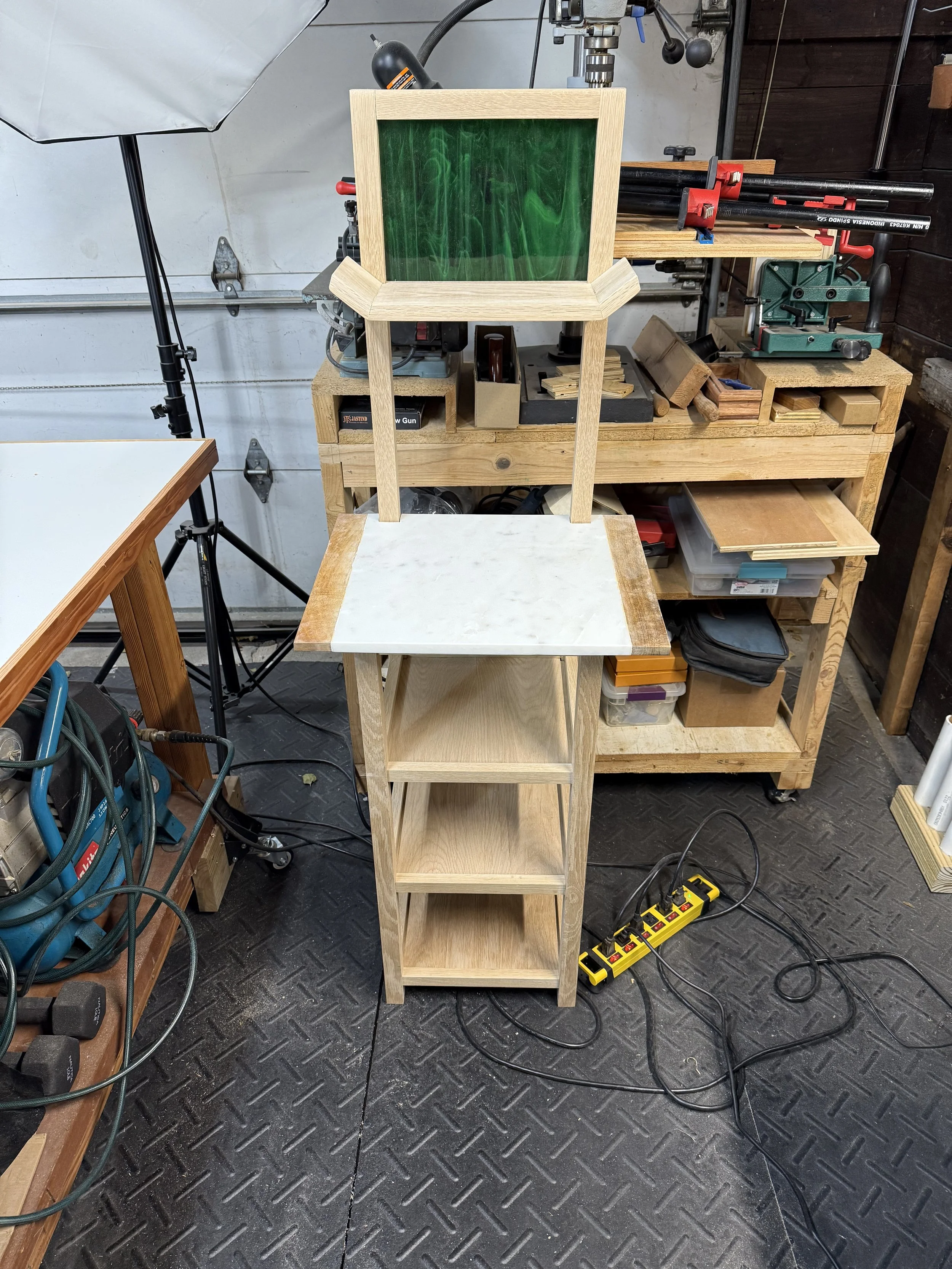 Workshop with a wooden table, a small stand with a marble top, a workbench with tools, and woodworking equipment.