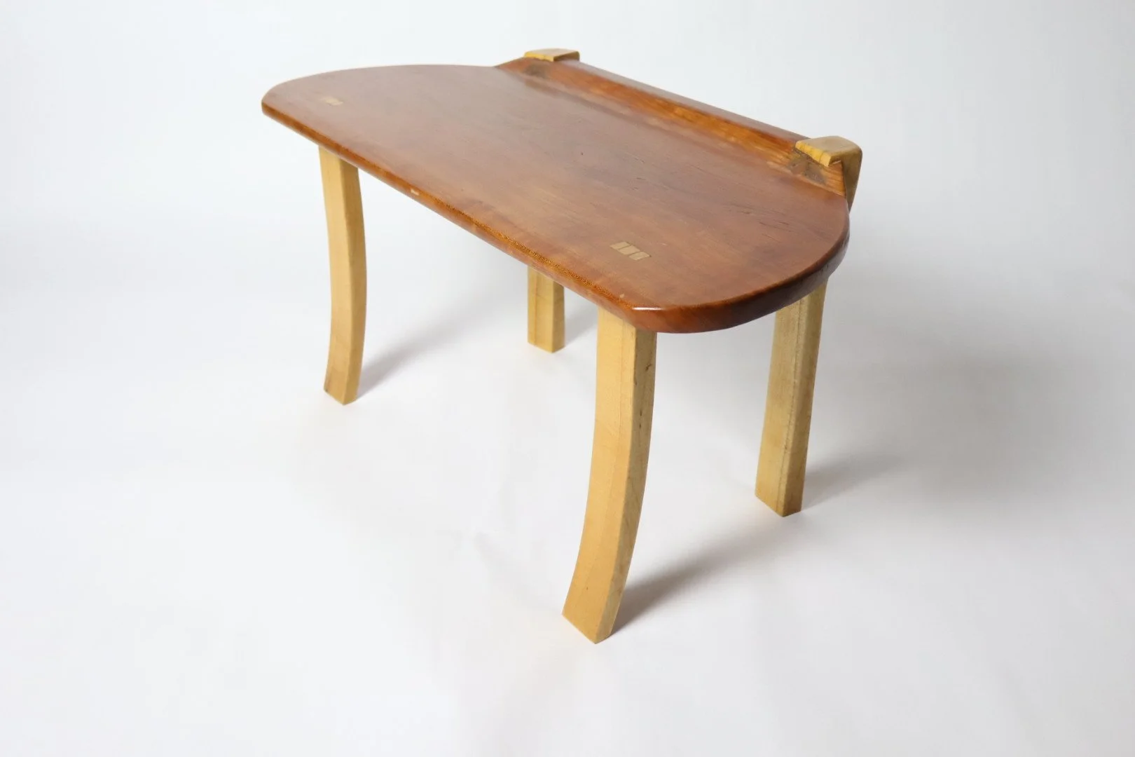 A small wooden table with a curved rectangular top and four legs, two of which are light wood and curved, and two are straight. The table is against a plain white background.