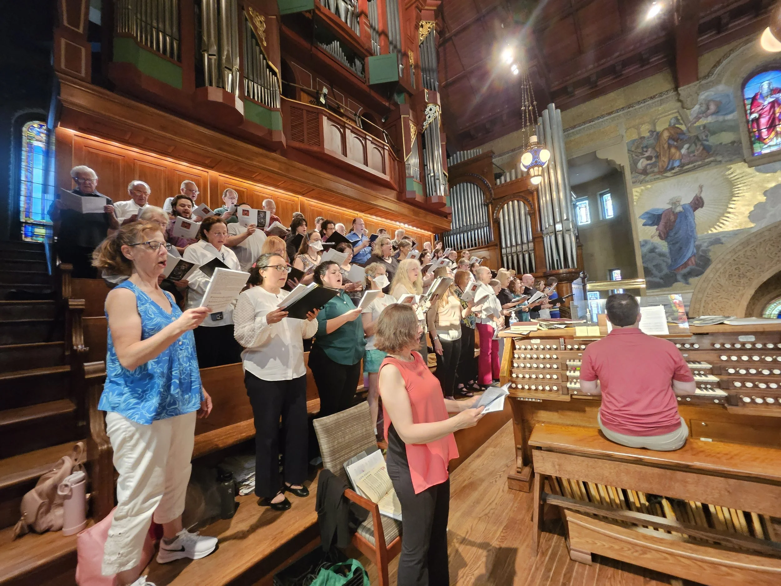 Choir members rehearsing at Stanford Memorial Chapel for Ascension Day service with large pipe organ and stained glass windows.