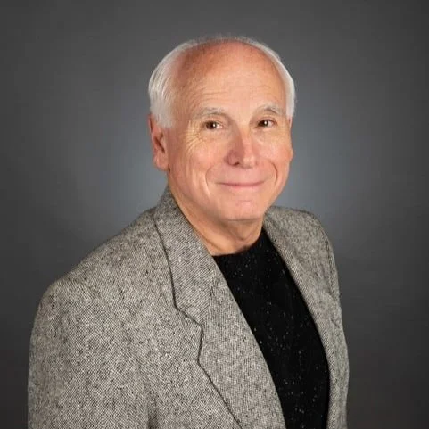 Paul Lovoi, senior warden, wearing a gray tweed blazer over a black shirt, smiling against a dark gray background.