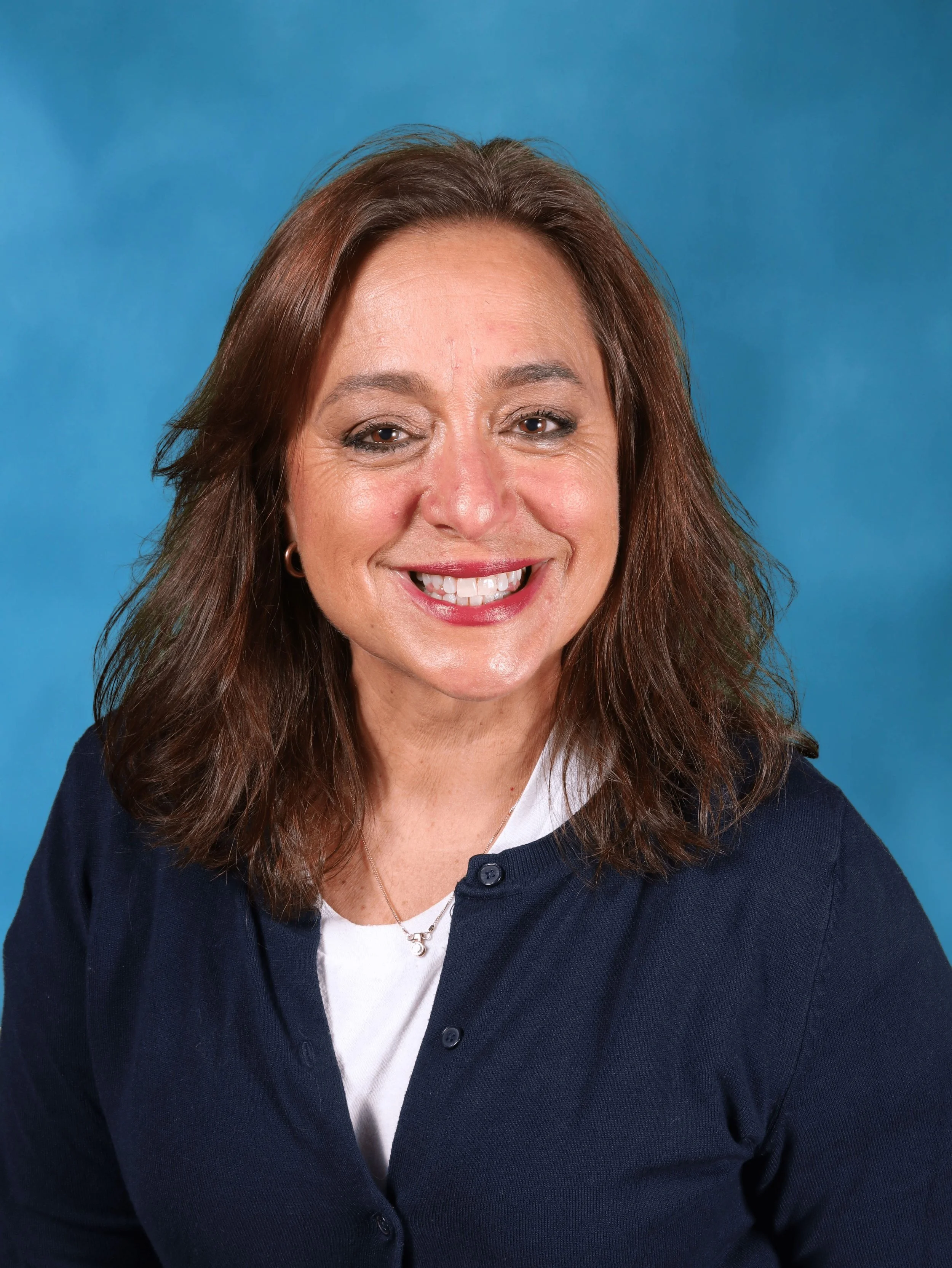 A woman with brown hair and a broad smile, our preschool director Cara O'Connell, wearing a navy cardigan over a white top, against a blue background.
