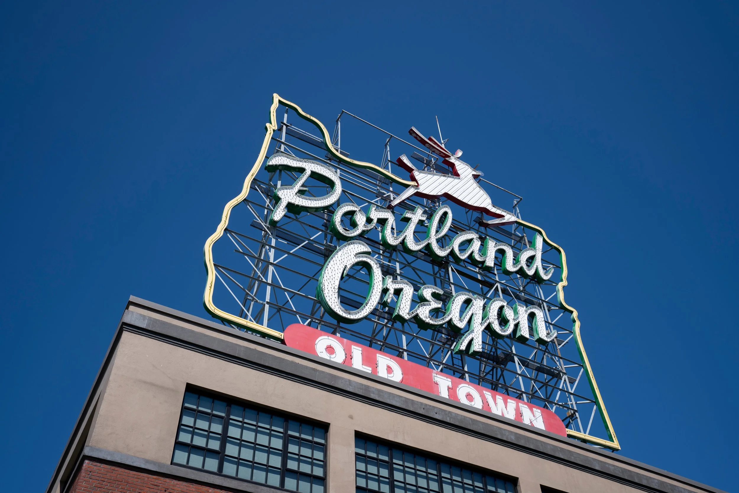 Neon sign reading Portand Oregon with an outline shape of the state of Oregon above it, and smaller text that says Old Town, set against a clear blue sky.