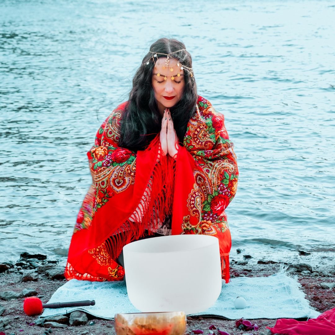 A person in a colorful shawl meditates by the water with a crystal singing bowl.