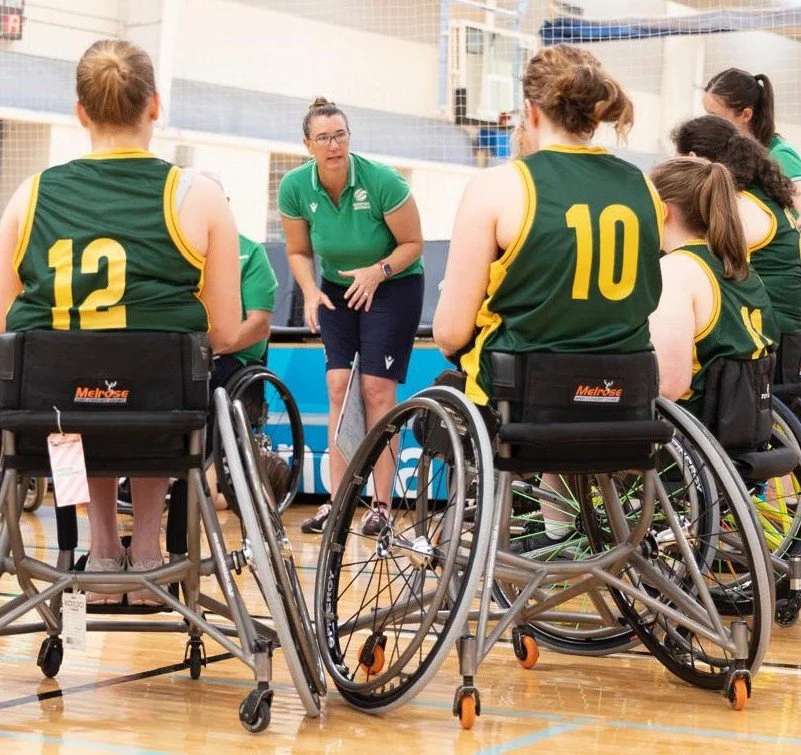 Wheelchair basketball team listening to coach during timeout in gymnasium.