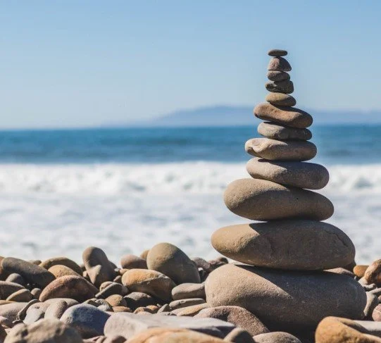 A stack of smooth stones balanced on the beach with the ocean and sky in the background.