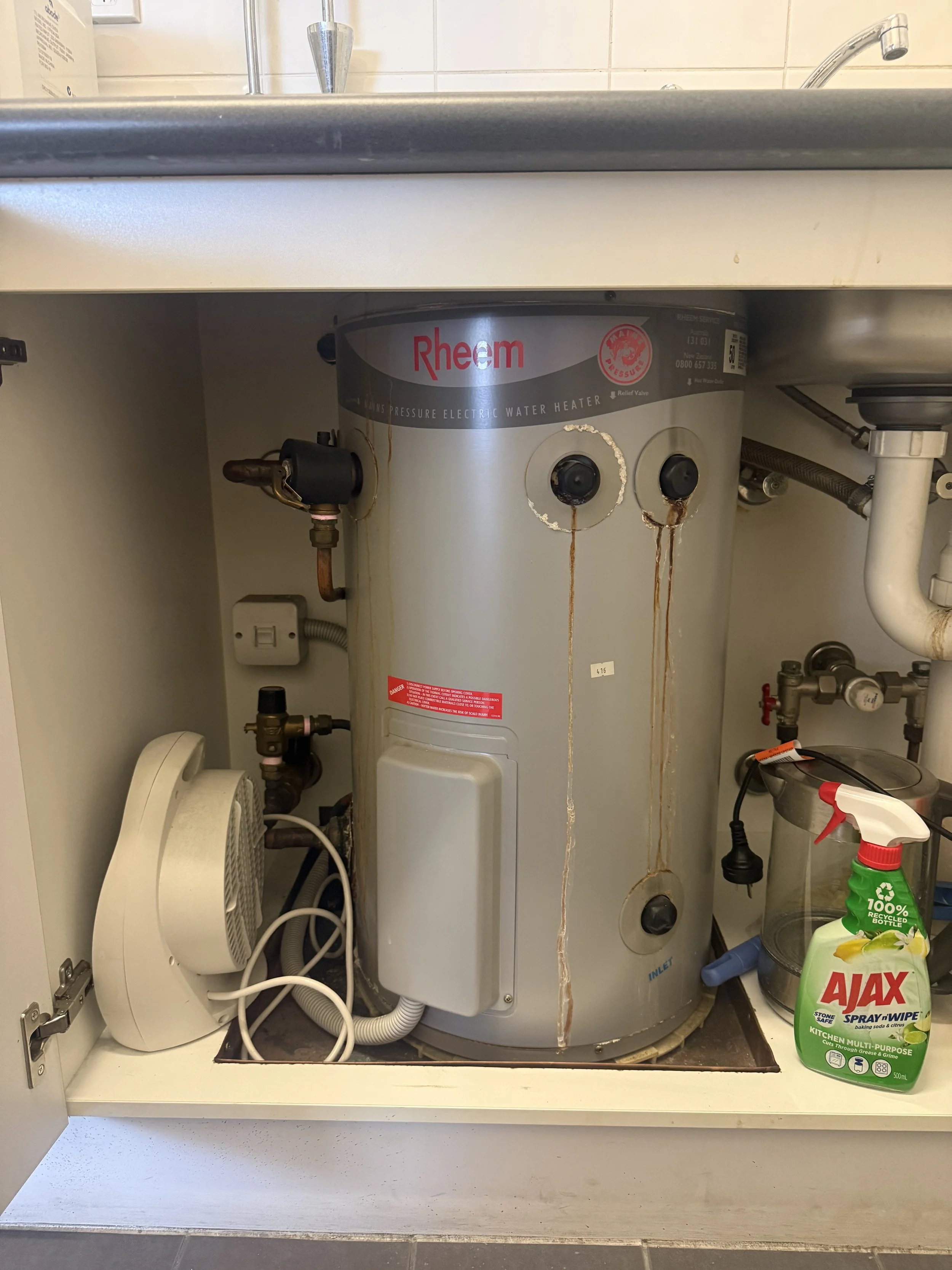 Under sink water heater with rust stains and a nearby spray bottle of Ajax cleaner.