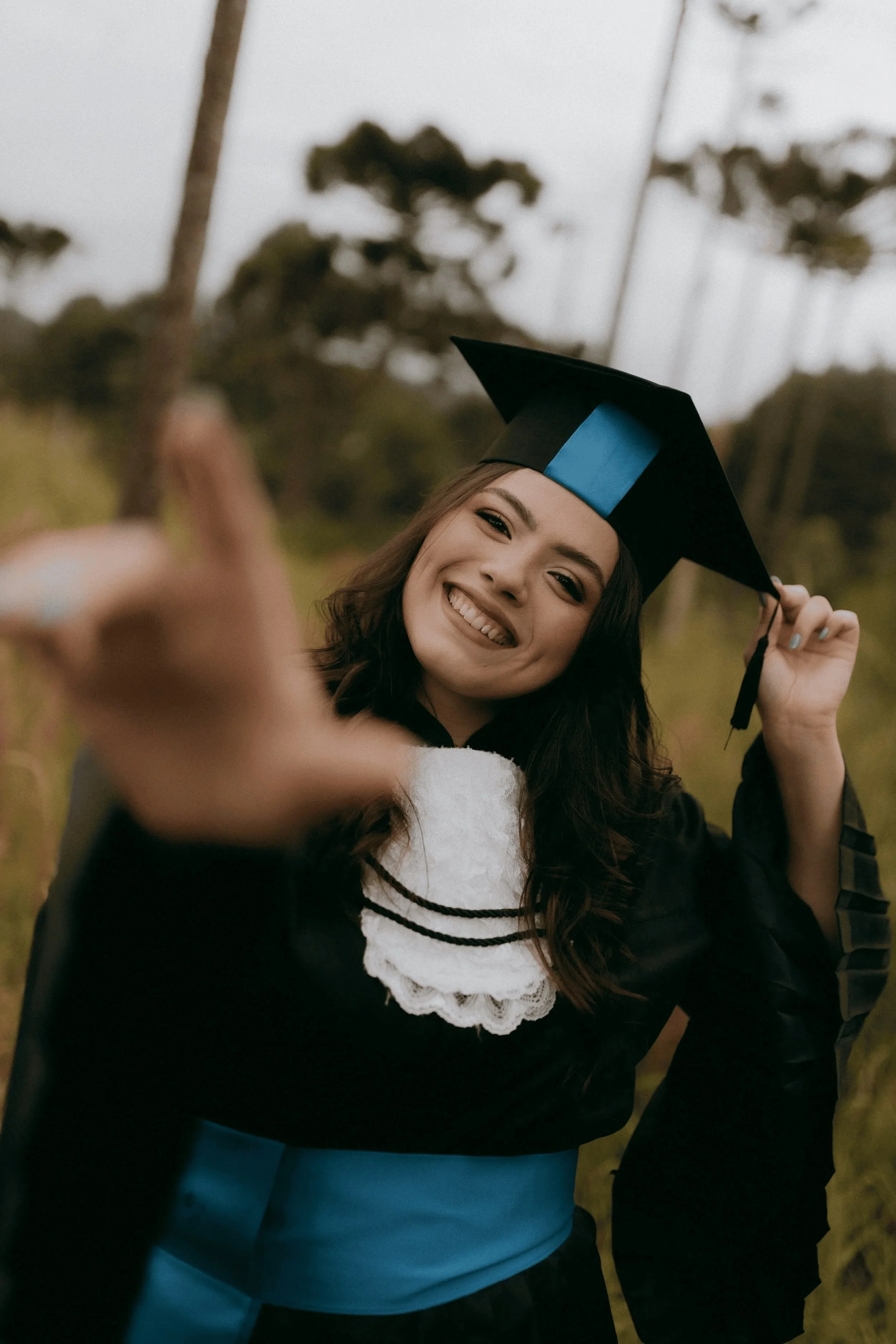 A young woman in a graduation cap and gown smiling and making a playful gesture towards the camera.