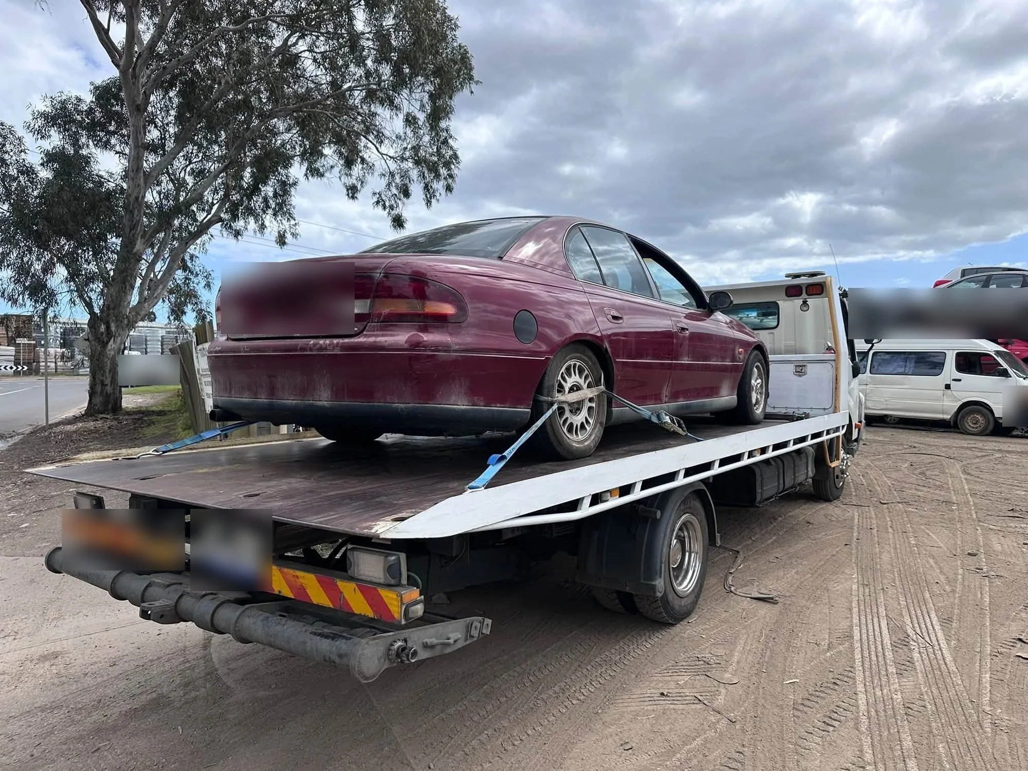 A weathered maroon Holden Commodore sedan strapped onto the deck of our white tilt tray truck