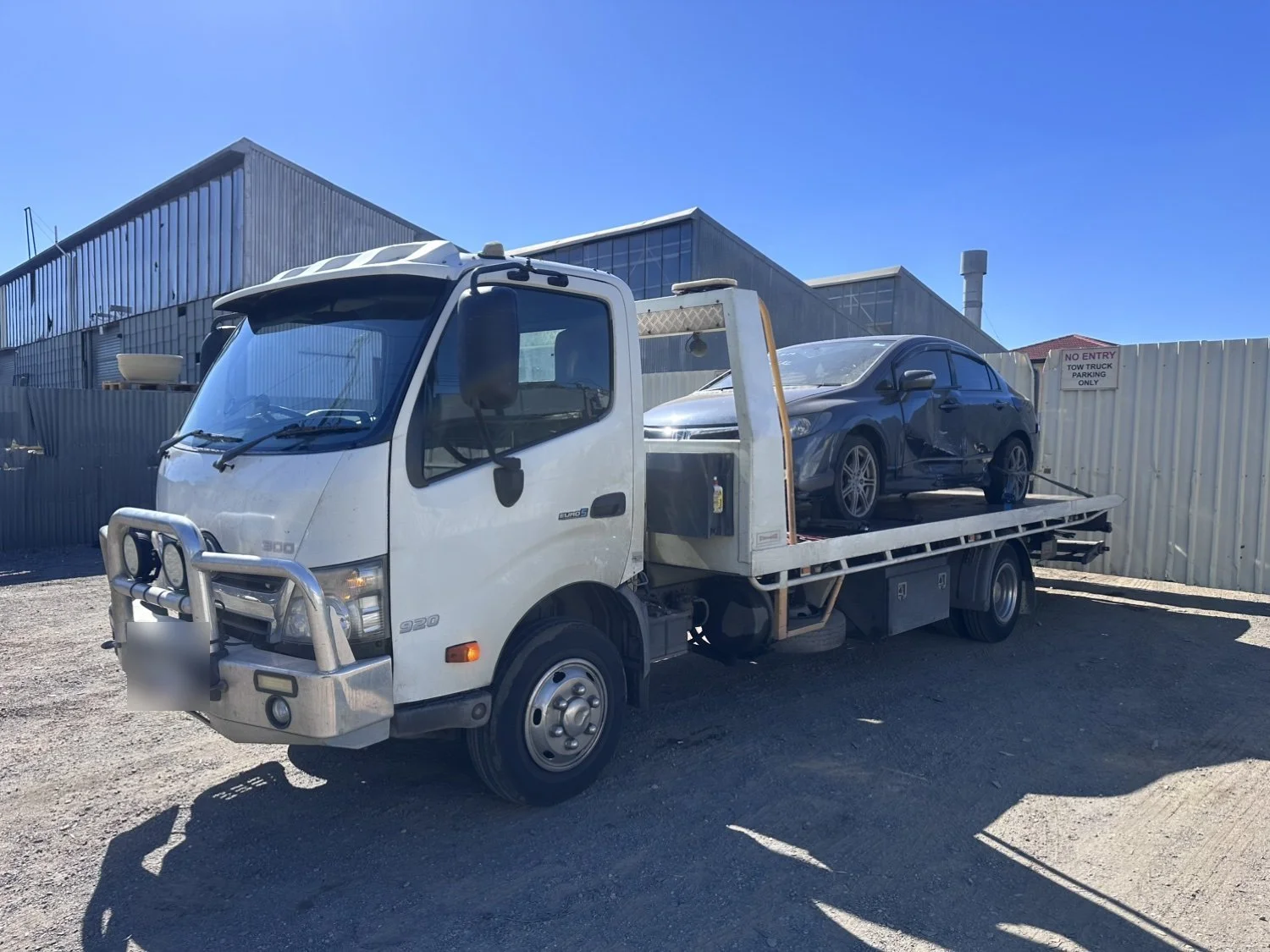 A dark Honda Civic sedan loaded on the deck of our white tilt tray tow truck