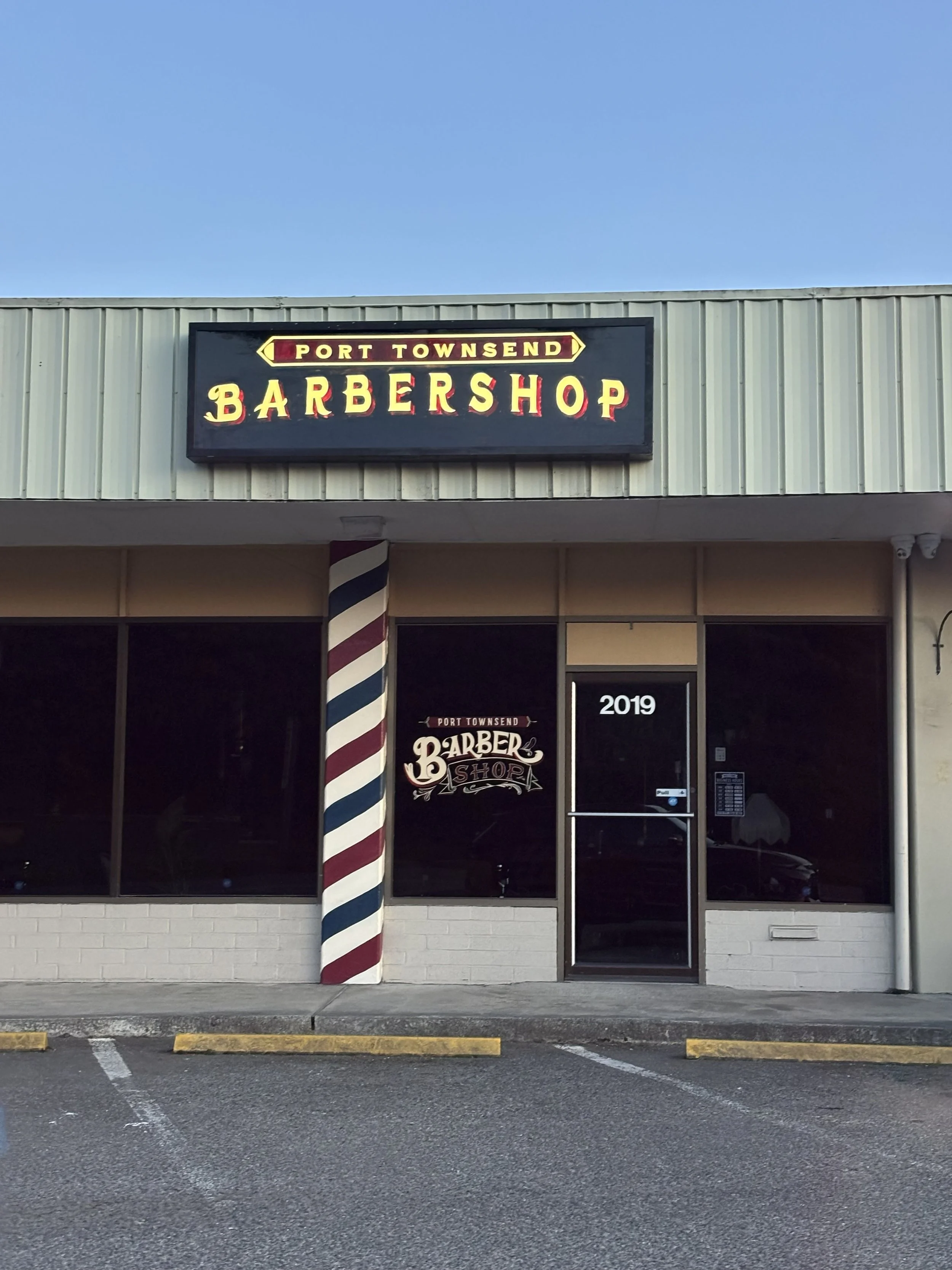Exterior of a barbershop with a sign that reads 'Port Townsend Barbershop' and a traditional barber pole in front.