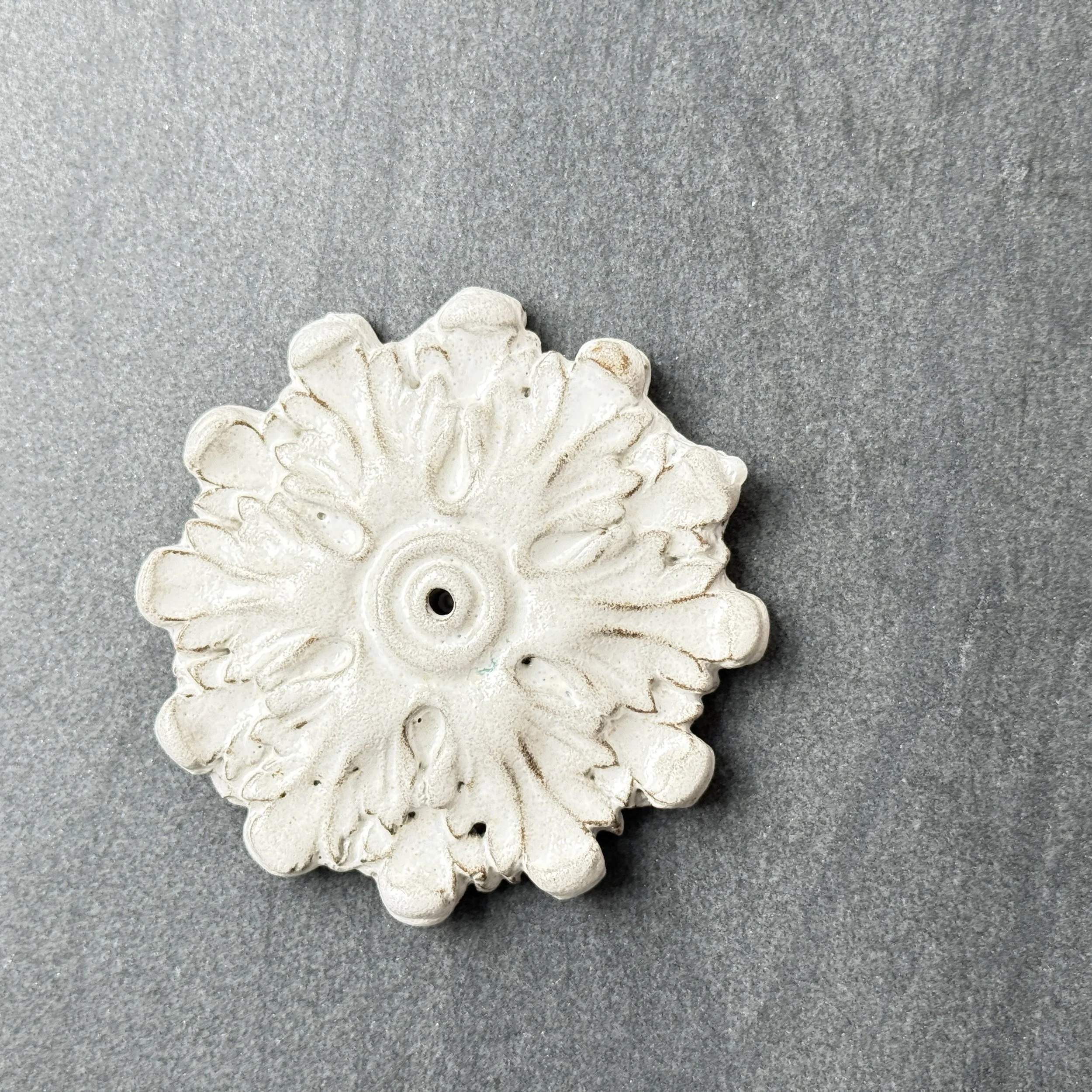 Close-up of a white decorative ceramic or plaster piece with floral and leaf patterns, resting on a gray surface.