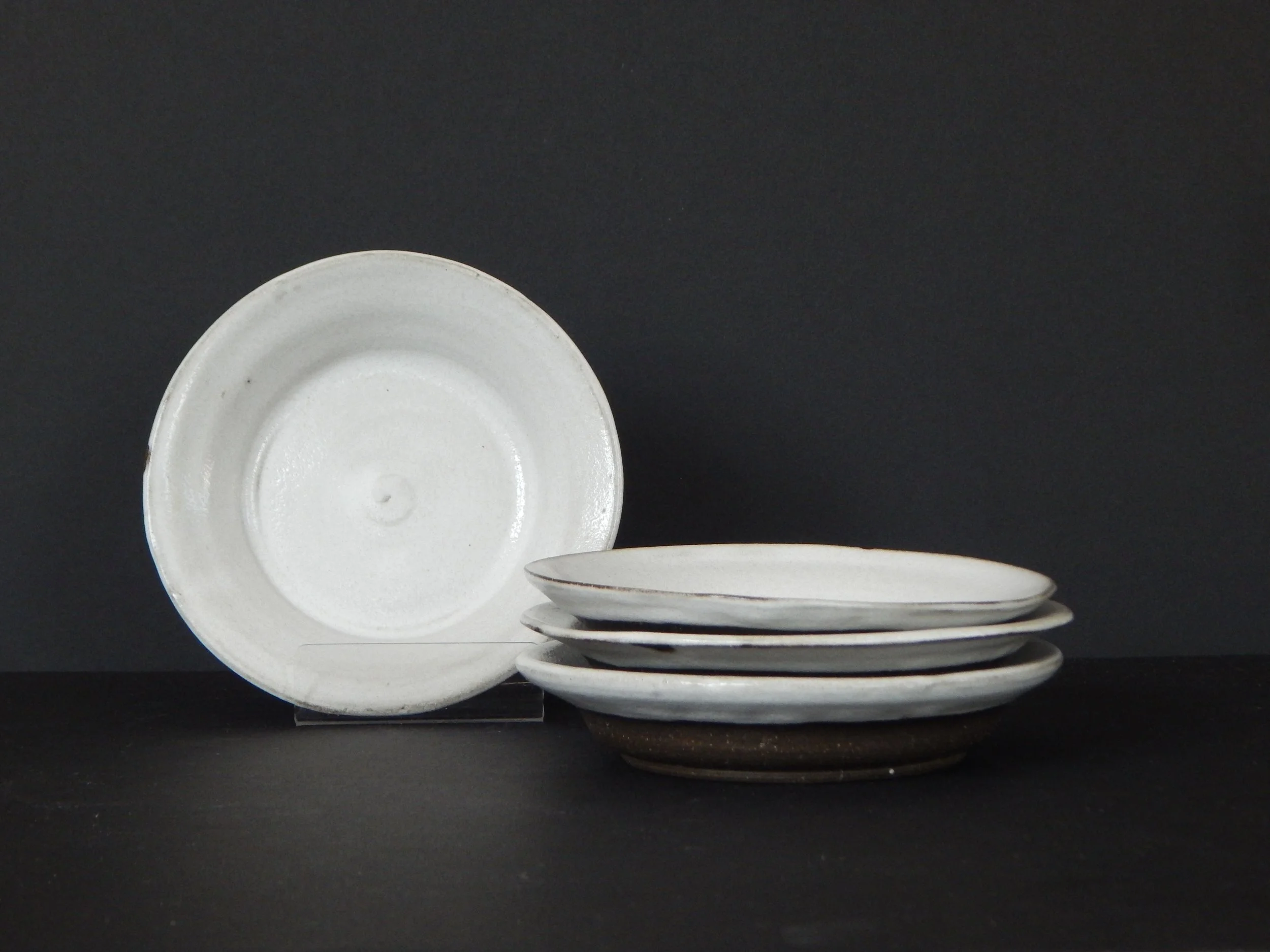 Small handmade white ceramic plate or saucer with matte glaze and dark clay base, approx. 5.75 inches wide