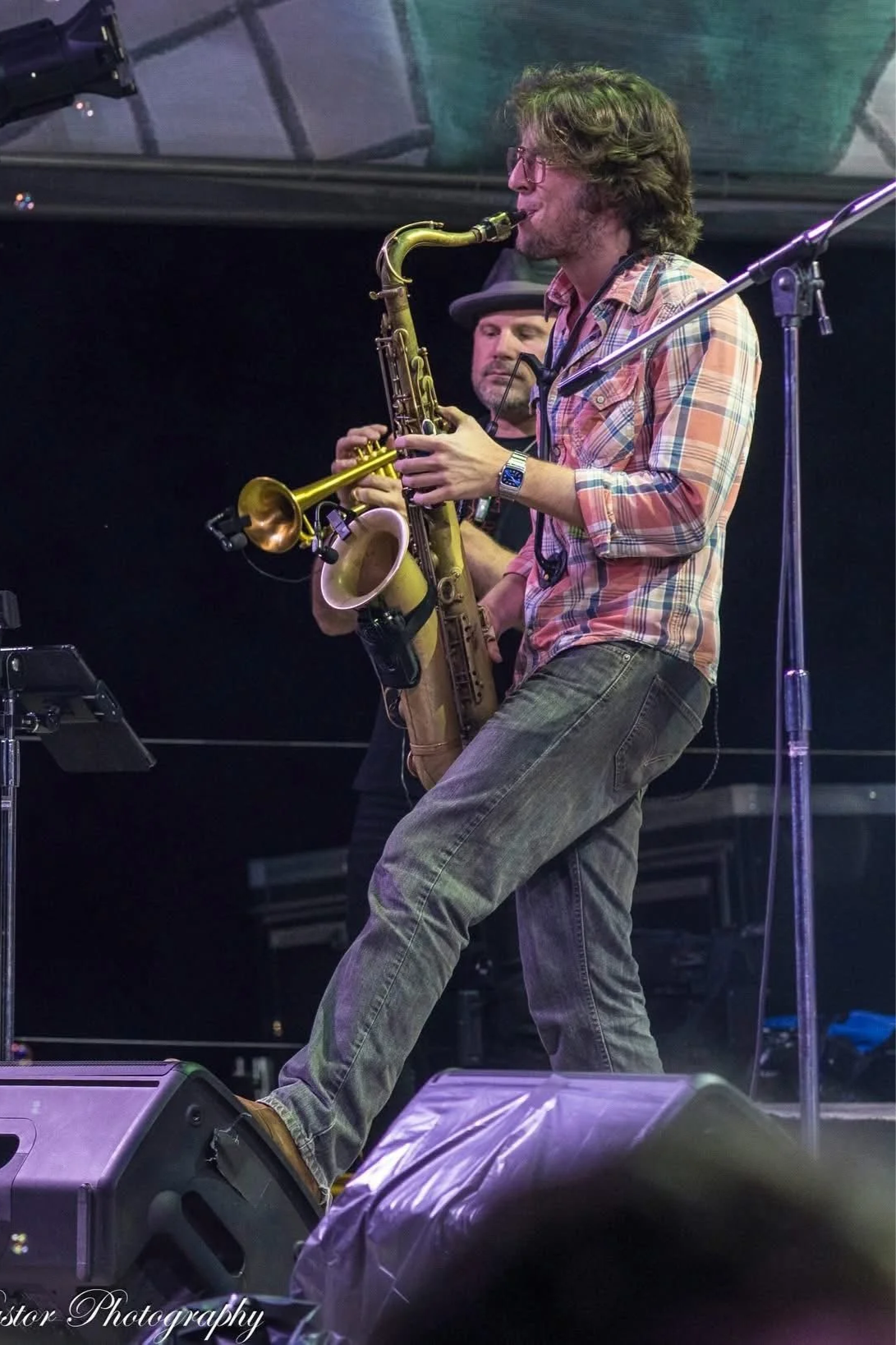 Live saxophone performance on a huge outdoor festival stage, featuring a professional saxophonist entertaining a large crowd under bright stage lights.