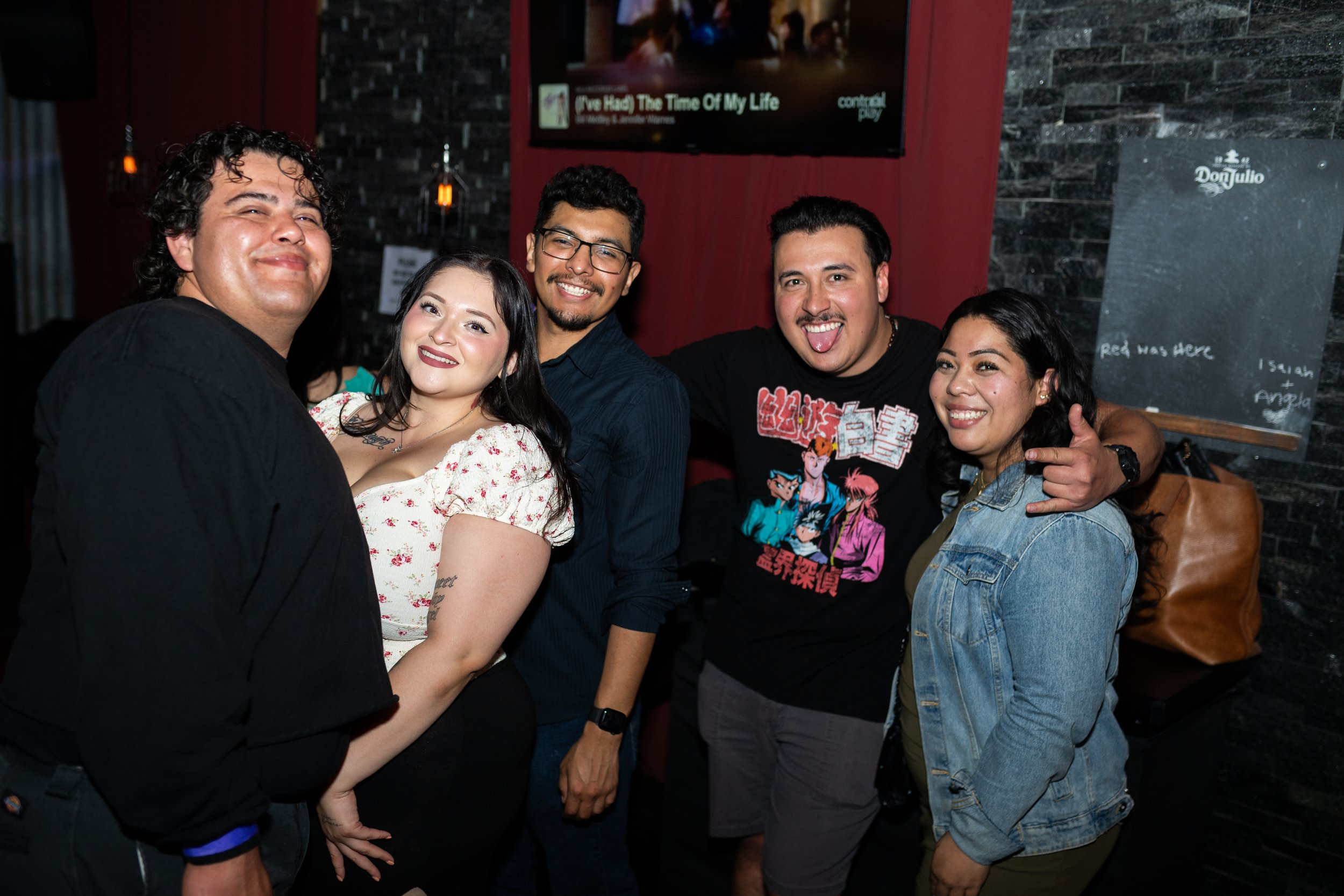 Group of five friends smiling and posing together at a bar or restaurant
