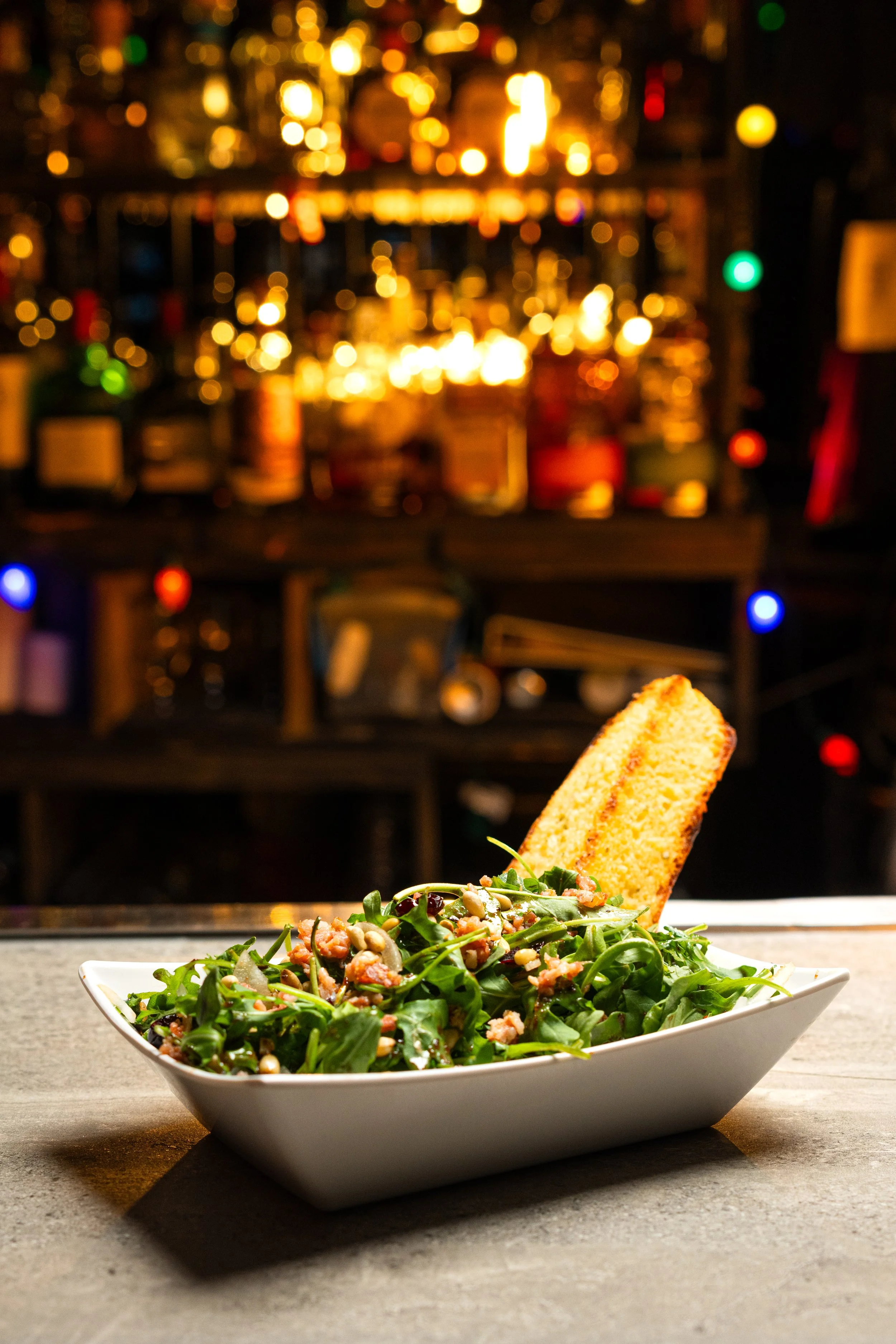 Salad with arugula and nuts in a white bowl on a bar counter.
