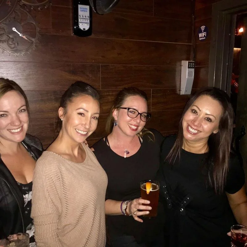 Group of women smiling at a bar, holding drinks.